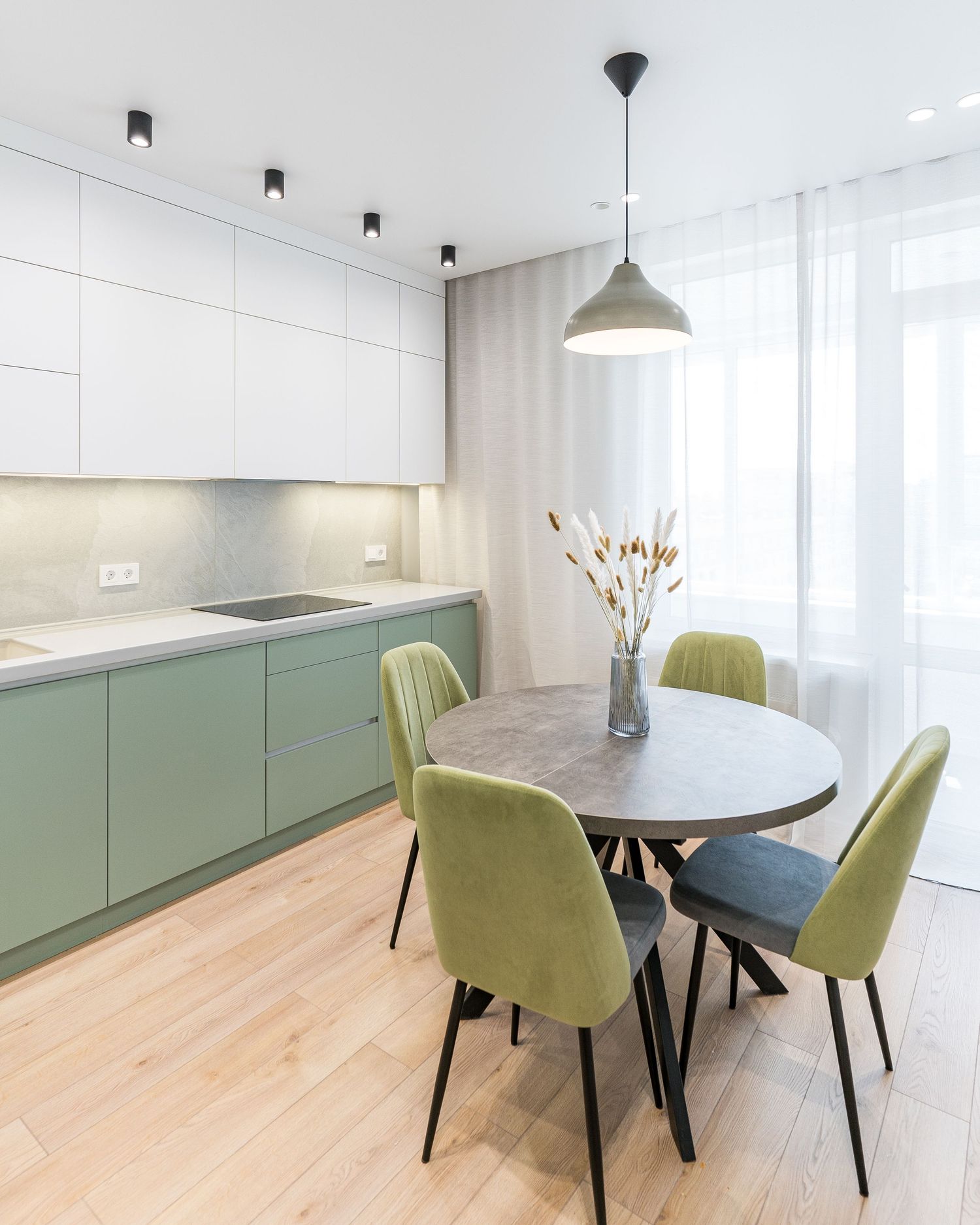 Sleek kitchen design with sage green base cabinets and round dining table with velvet chairs.