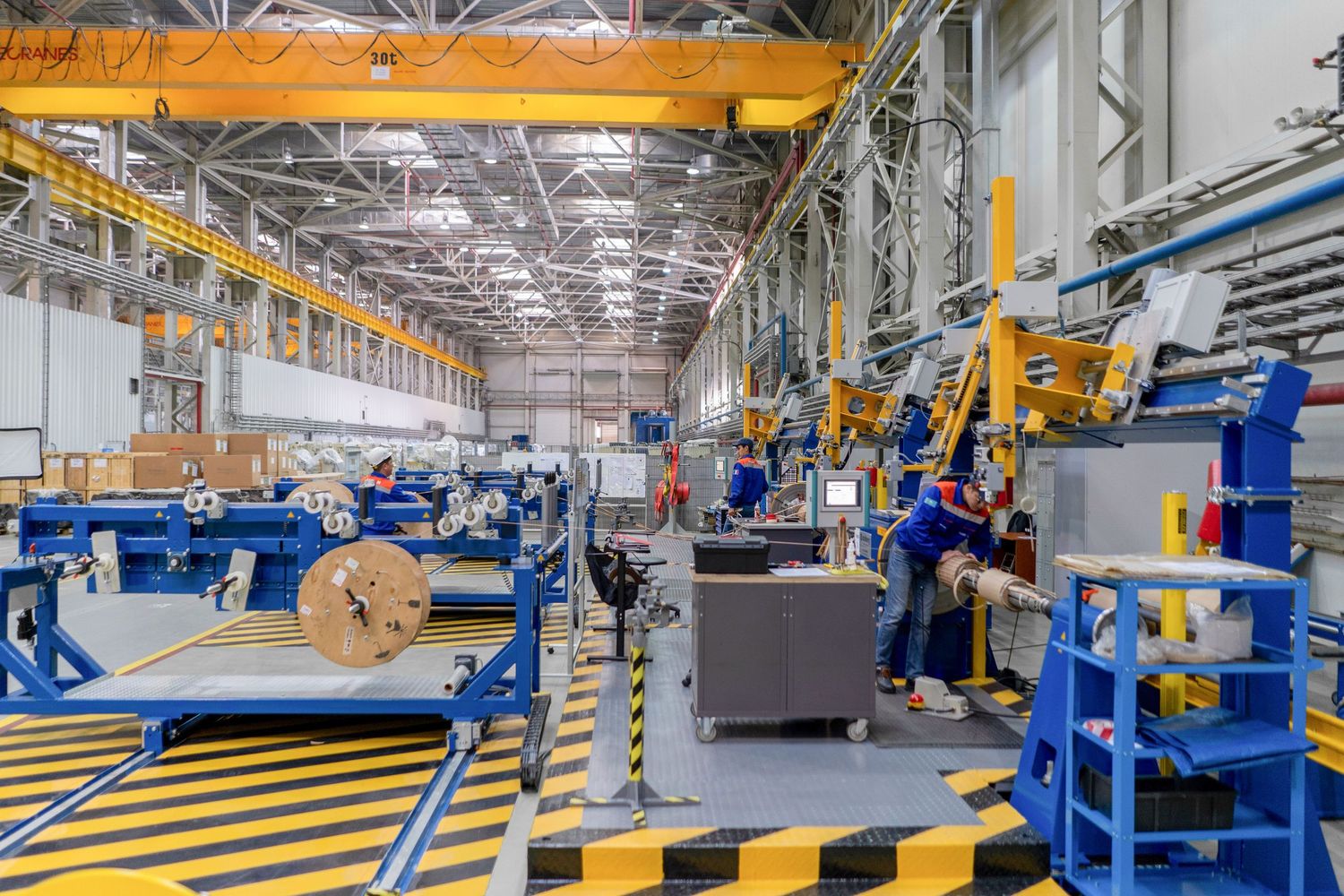 Large industrial warehouse with overhead cranes and manufacturing equipment arranged in production lines.