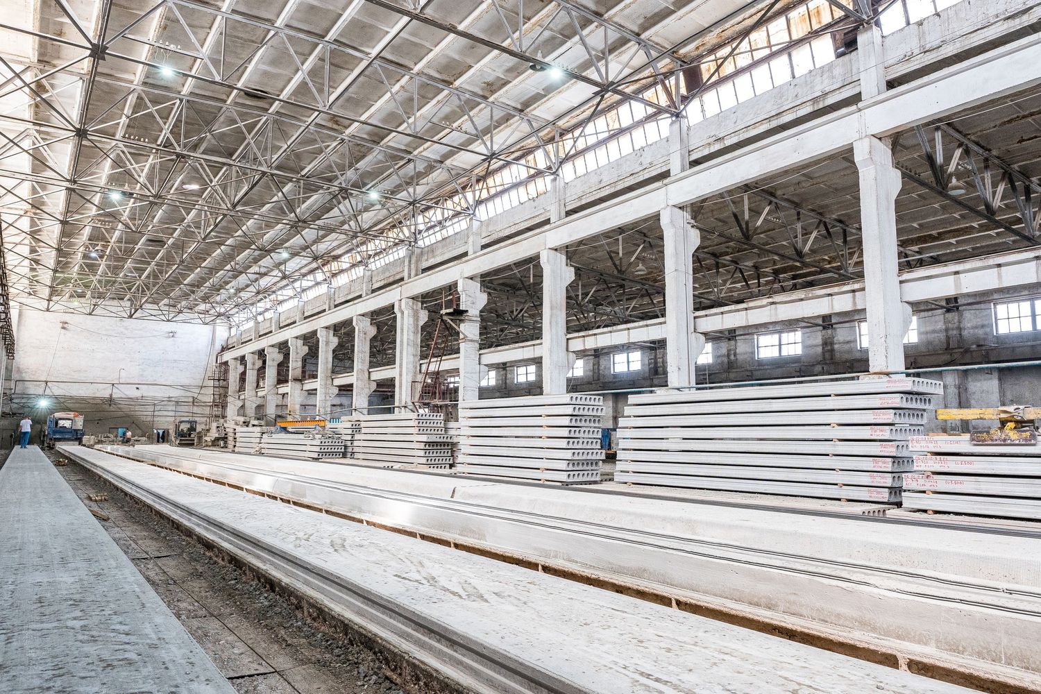 Industrial warehouse interior with rows of concrete production equipment and machinery.