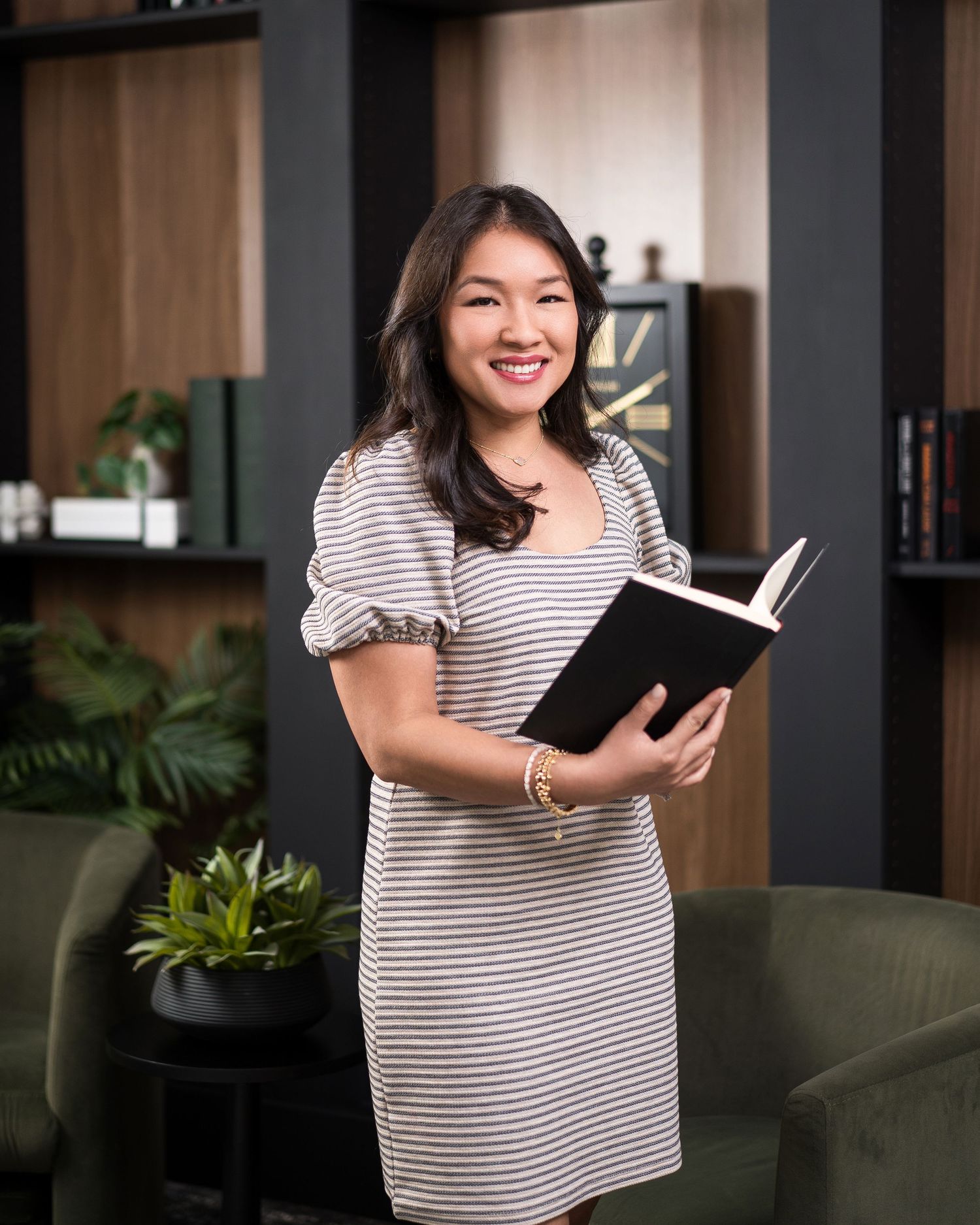 Woman in striped shirt reading book in modern interior setting with plants.