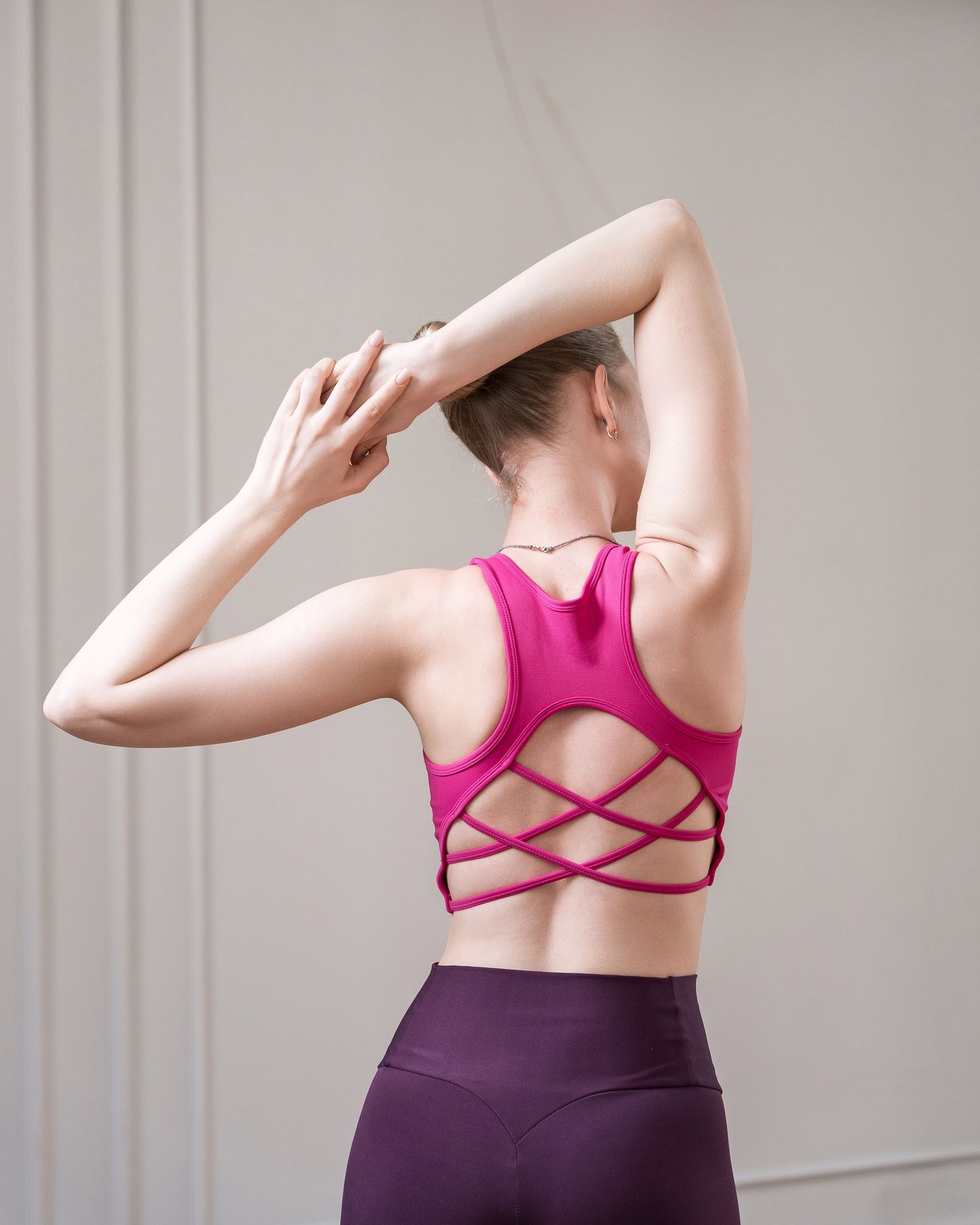 Person in pink sports top and purple leggings stretching backwards.