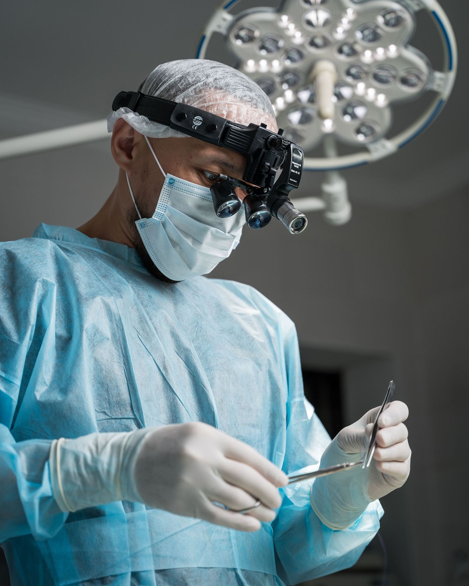 Surgeon wearing magnifying loupes and protective gear performing delicate operation.