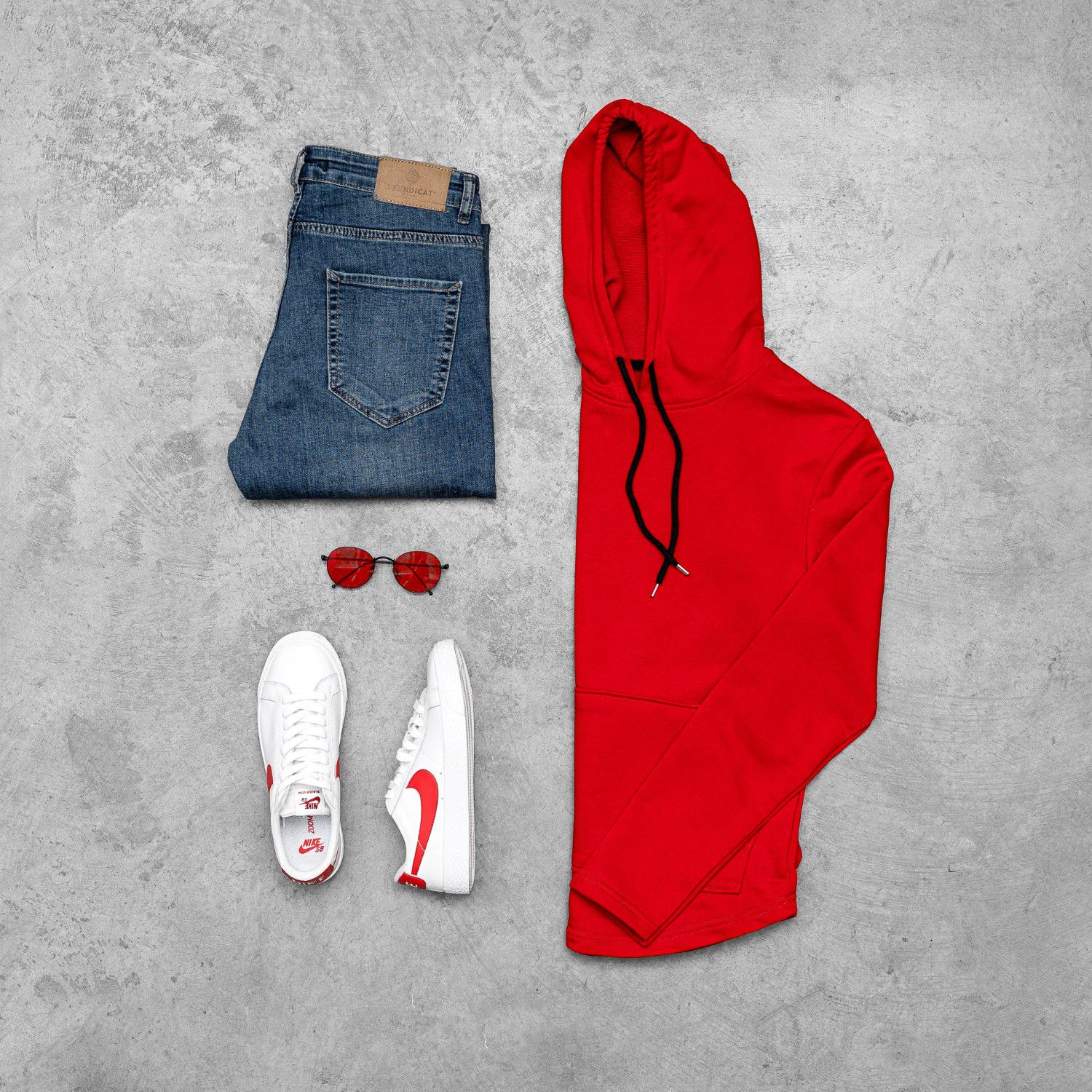 Casual outfit flat lay with red hoodie, blue jeans, white sneakers and sunglasses.