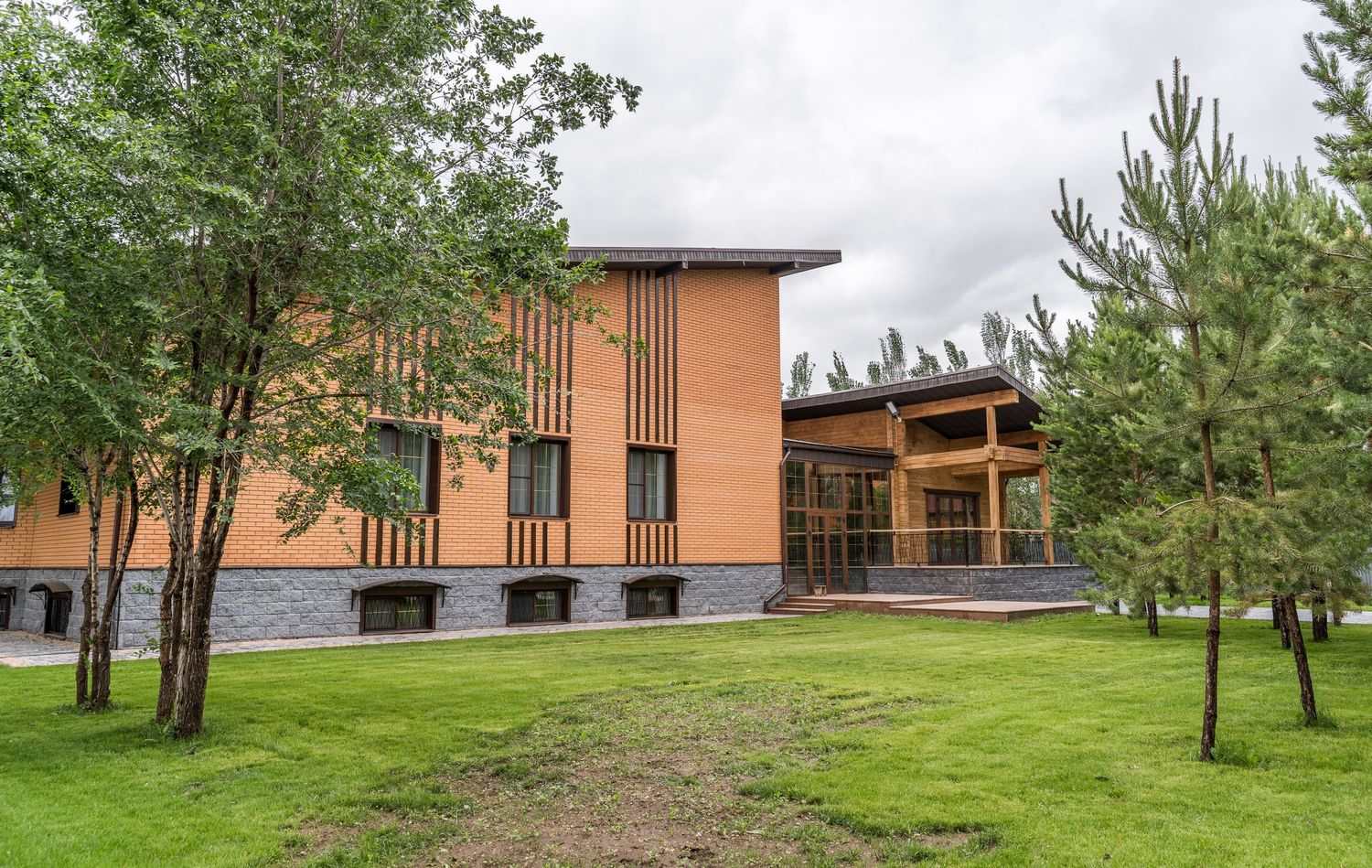 Scenic view of a wooden pavilion with natural landscaping and pine trees on a cloudy day.
