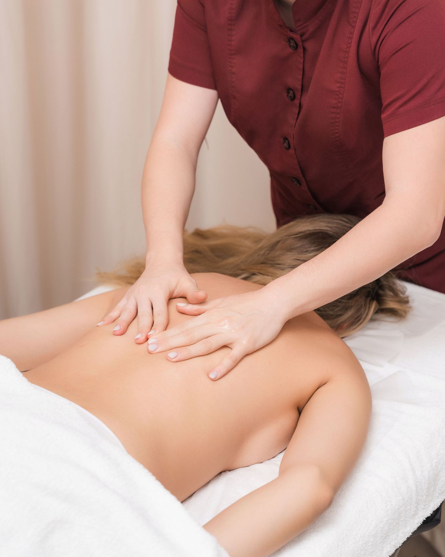 Massage therapist in burgundy uniform performing professional leg massage treatment.