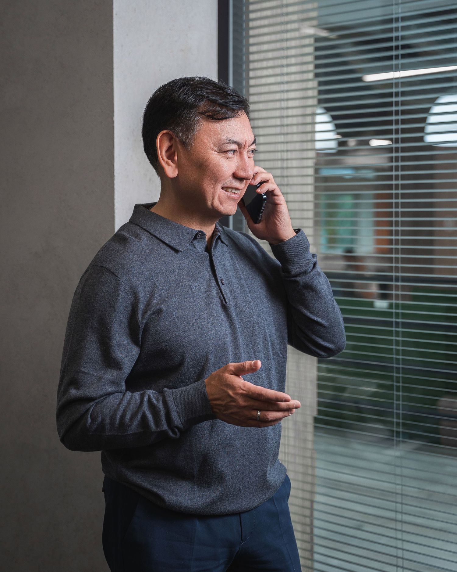 Business person in dark attire speaking on mobile phone by office window.