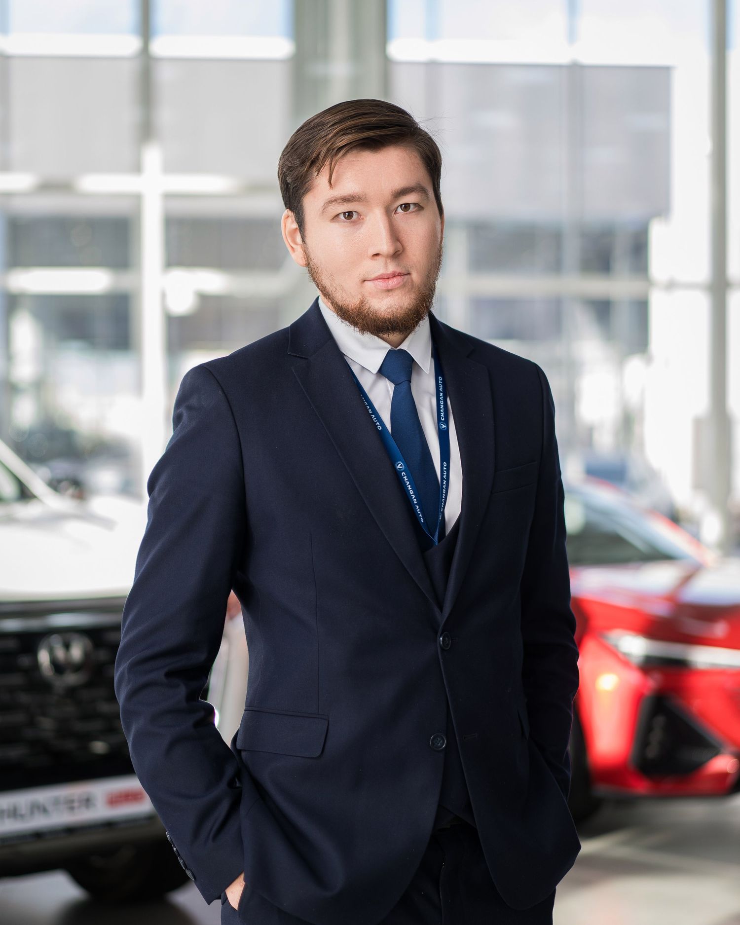 Professional in navy suit standing in modern car dealership showroom.