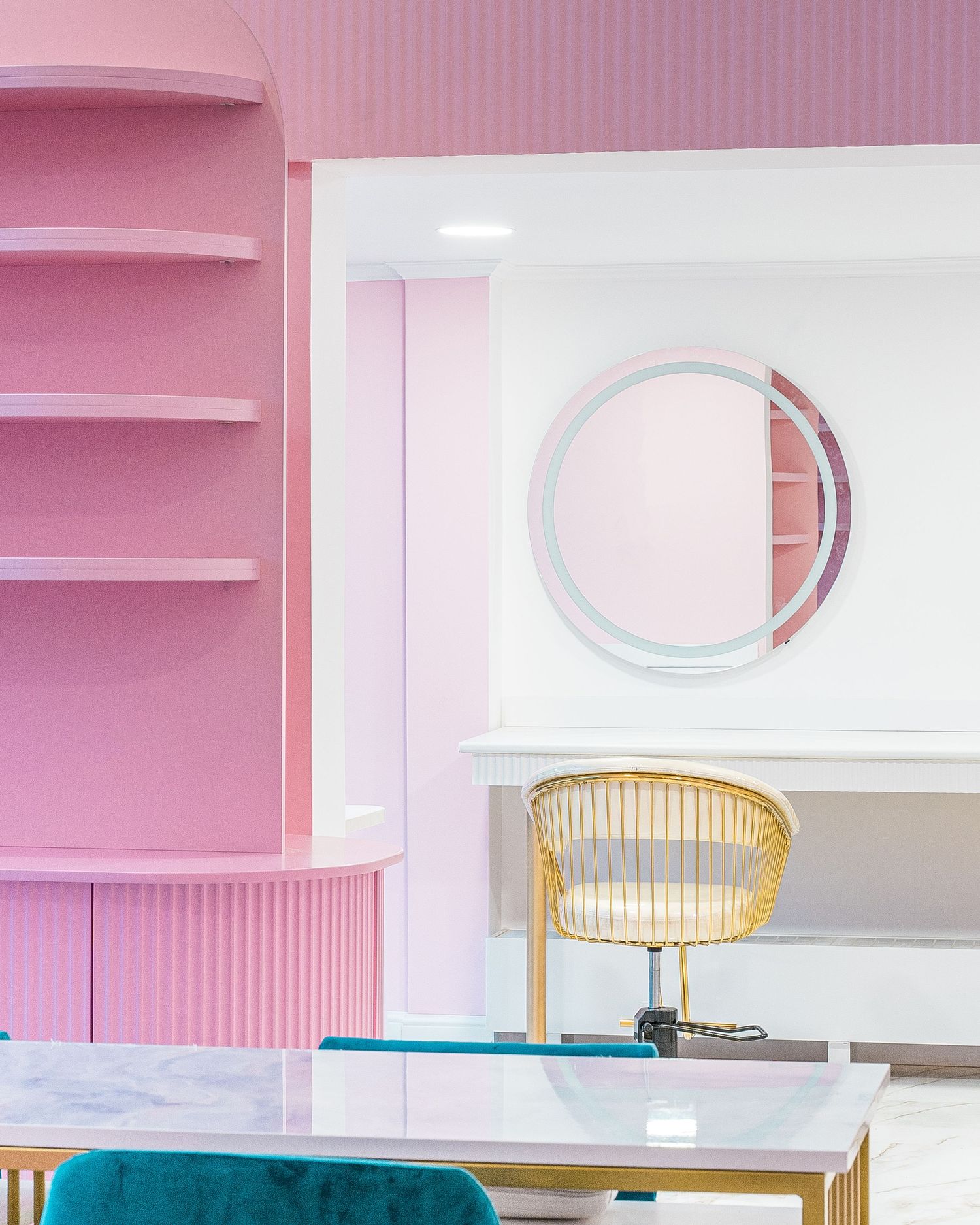 Modern pink interior with teal velvet seating, gold fixtures, and circular wall mirrors.
