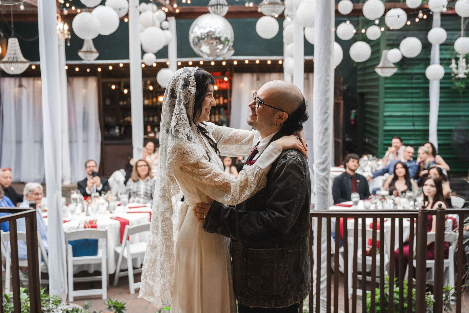 Bride and groom share first dance at outdoor wedding reception with string lights and disco ball.