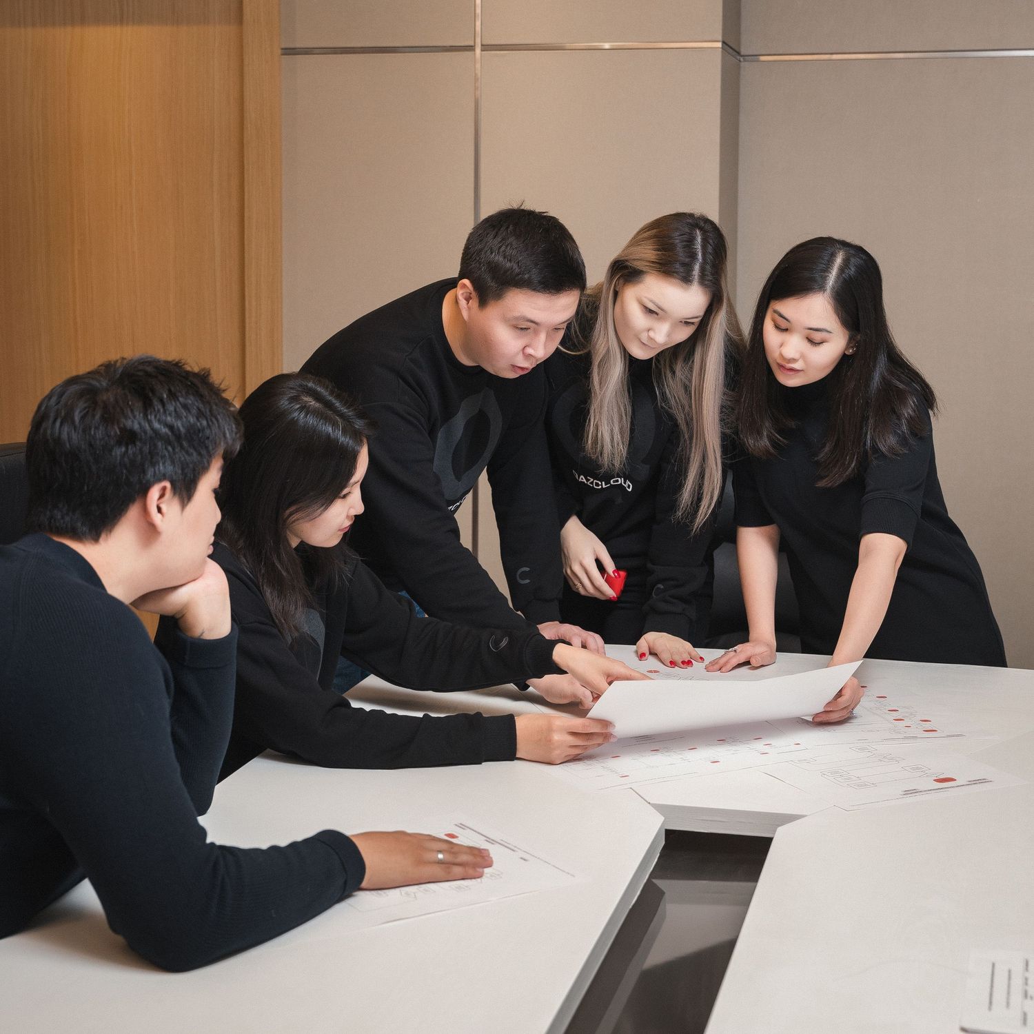 Team members in black attire gathered around table reviewing documents together.