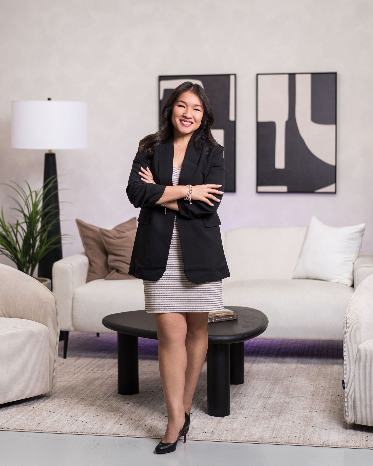 Woman in business attire posing confidently in modern white living room setting.