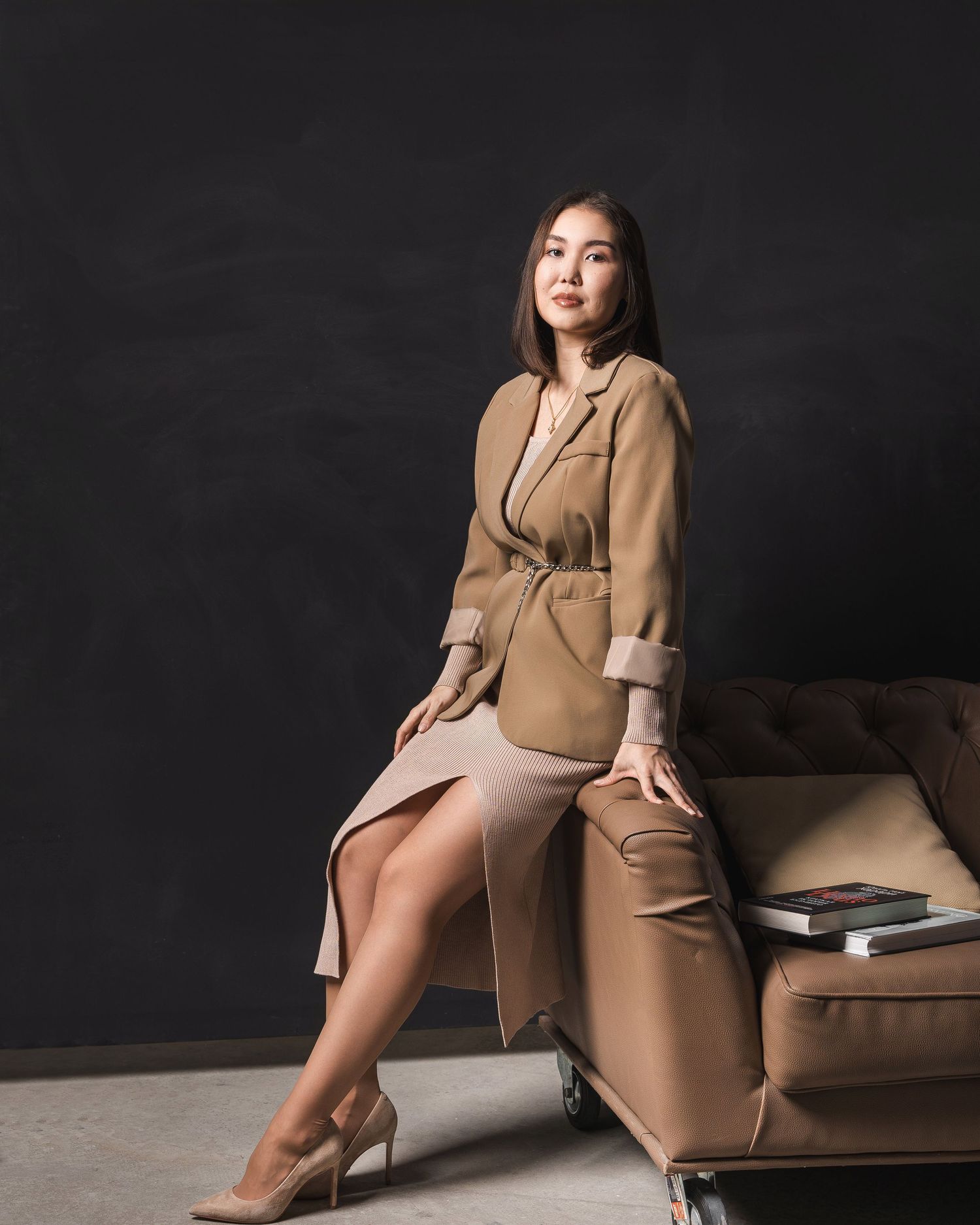 Stylish portrait session featuring tan coat and elegant poses on dark couch.