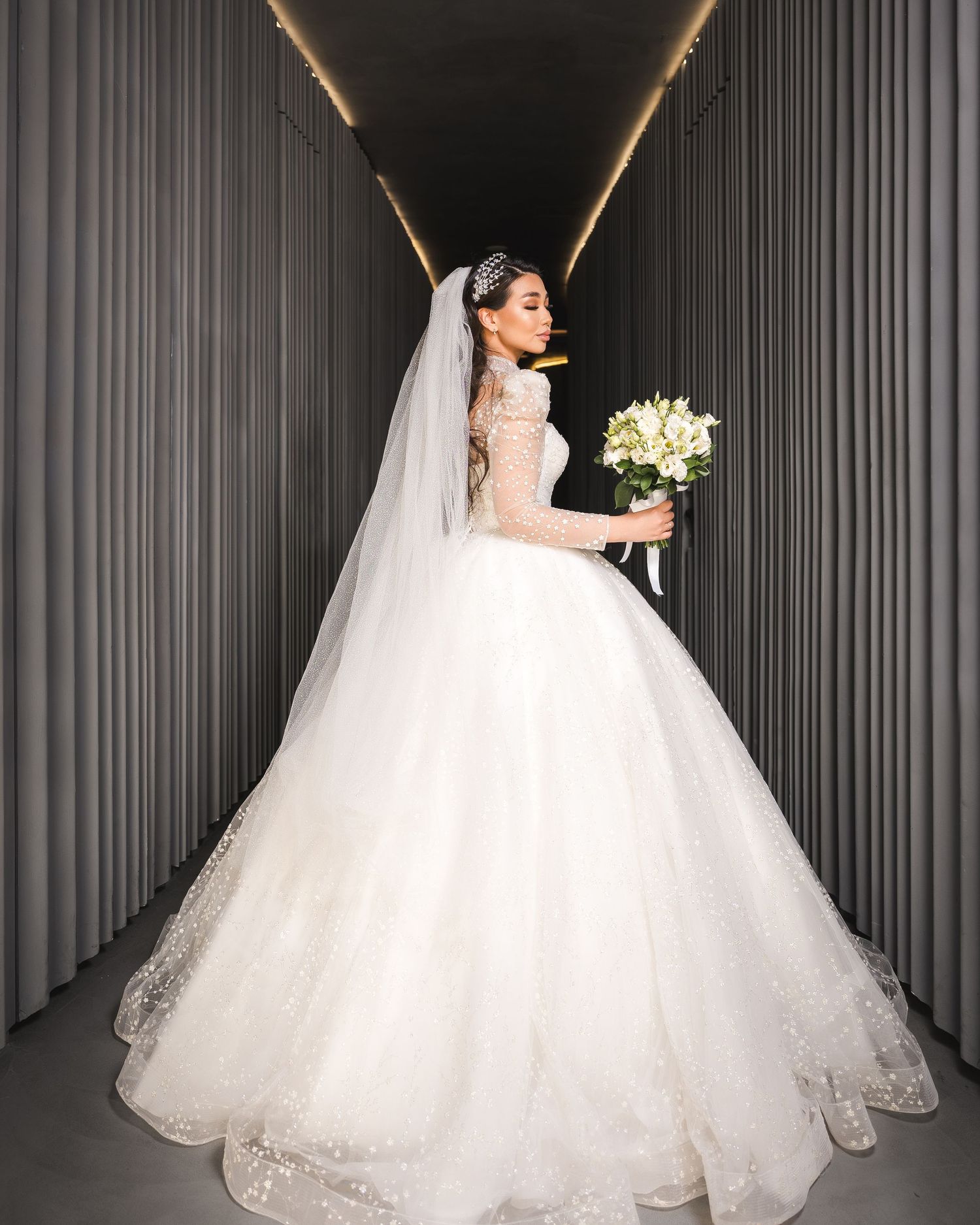 Bride in a white ballgown wedding dress with lace sleeves, cathedral veil, and floral bouquet.