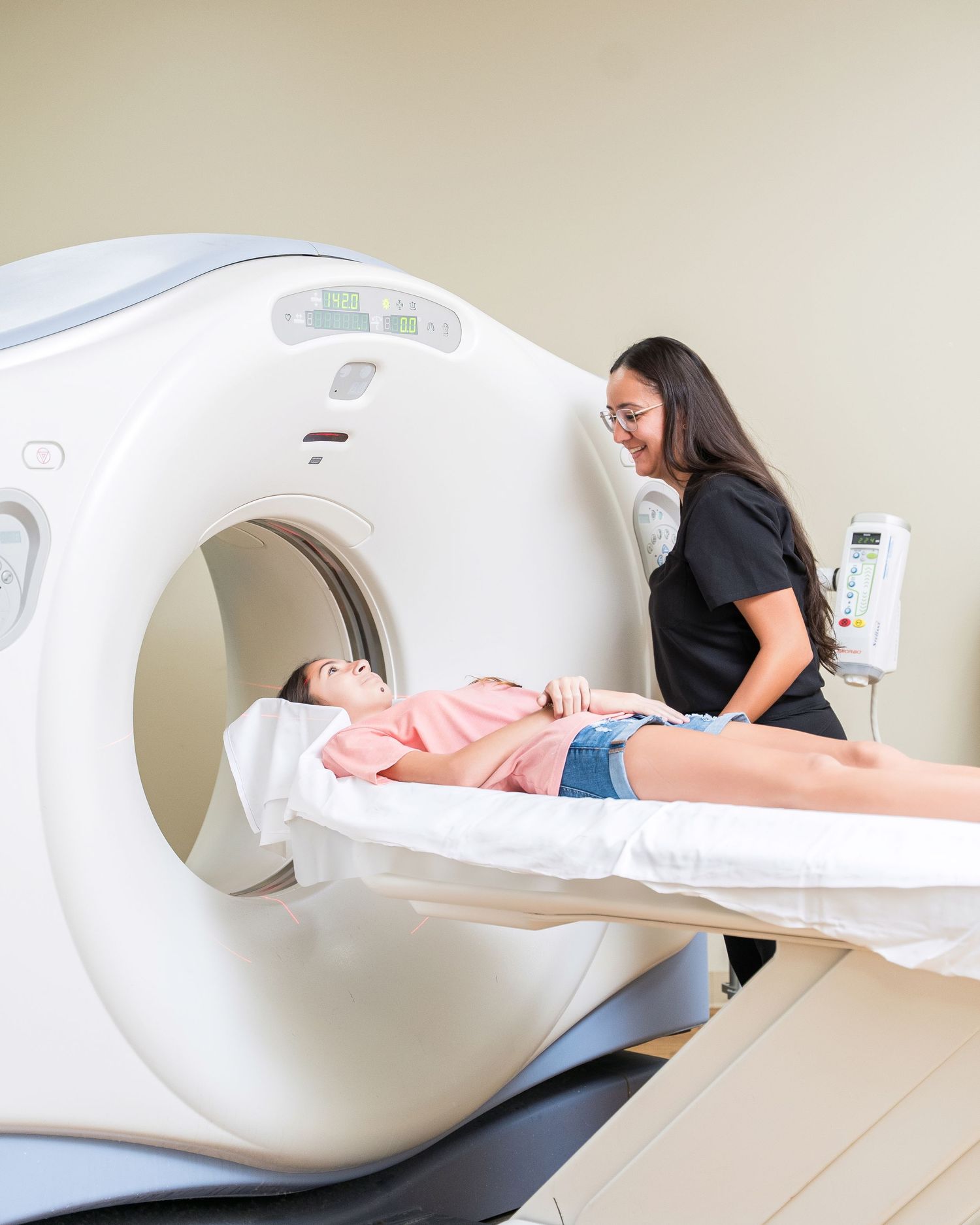 Medical technician operating CT scanner with patient on examination table.