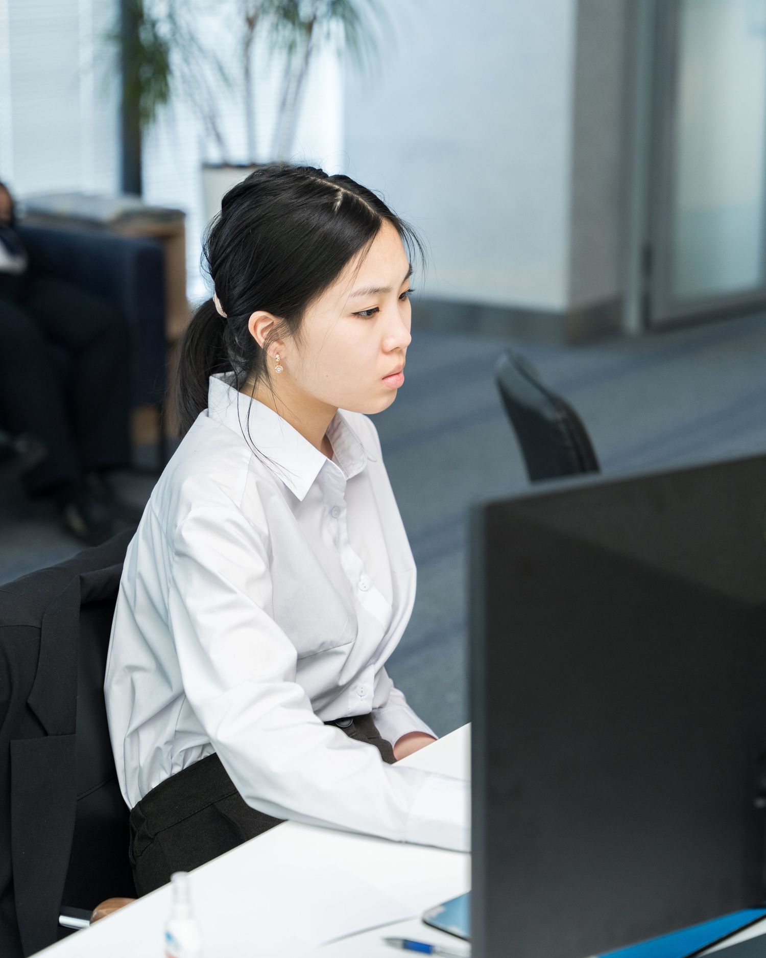 Office worker in white shirt focused on computer screen at modern workstation.