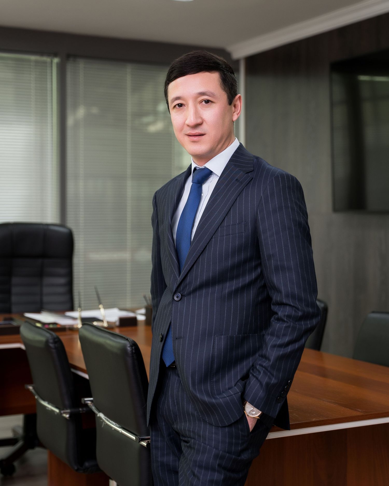 Executive in navy pinstripe suit poses confidently in modern office boardroom.