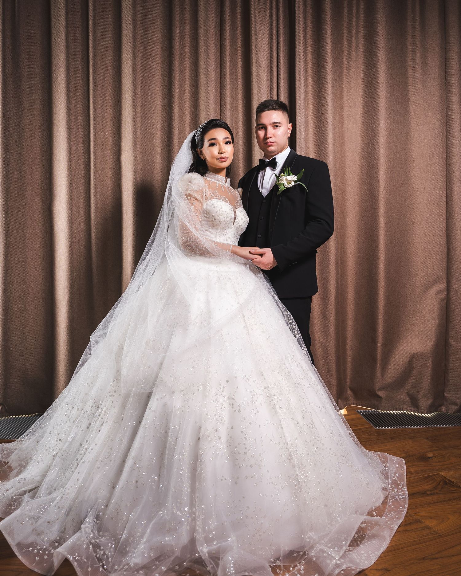 Couple poses in elegant wedding attire, bride in voluminous ball gown with veil, groom in black tuxedo.