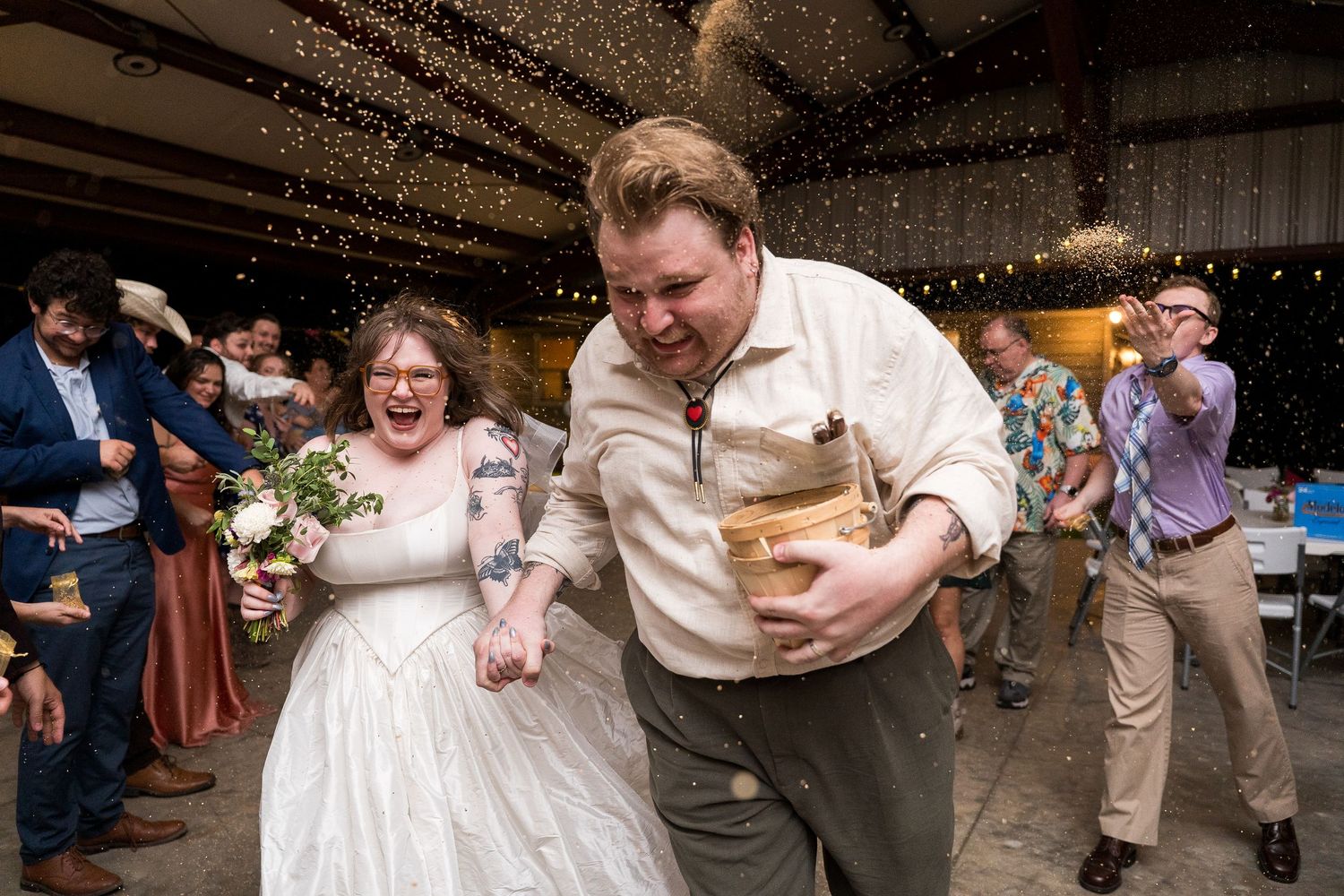 Joyful bride and groom exit wedding reception amid shower of rice, bride holding bouquet.
