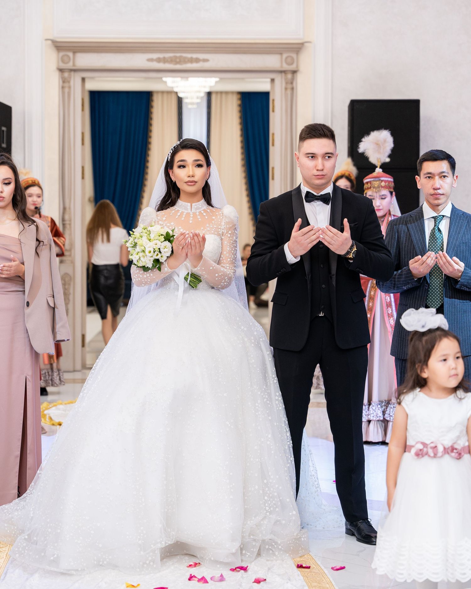 Bride and groom walk aisle in white lace ballgown and tuxedo during traditional wedding ceremony with guests.