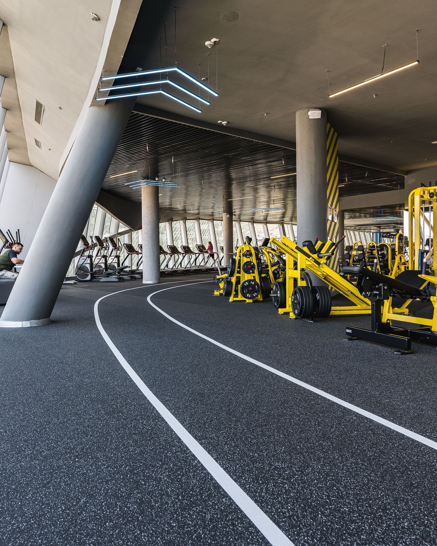 Spacious gym floor with curved track lines and yellow fitness equipment along the perimeter.