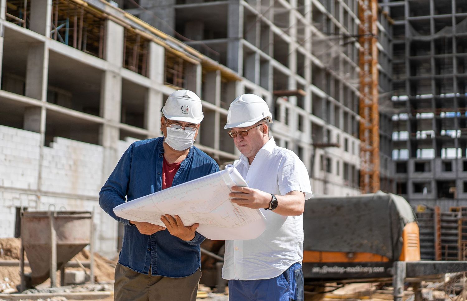 Construction site inspection with workers reviewing blueprints near concrete structure.