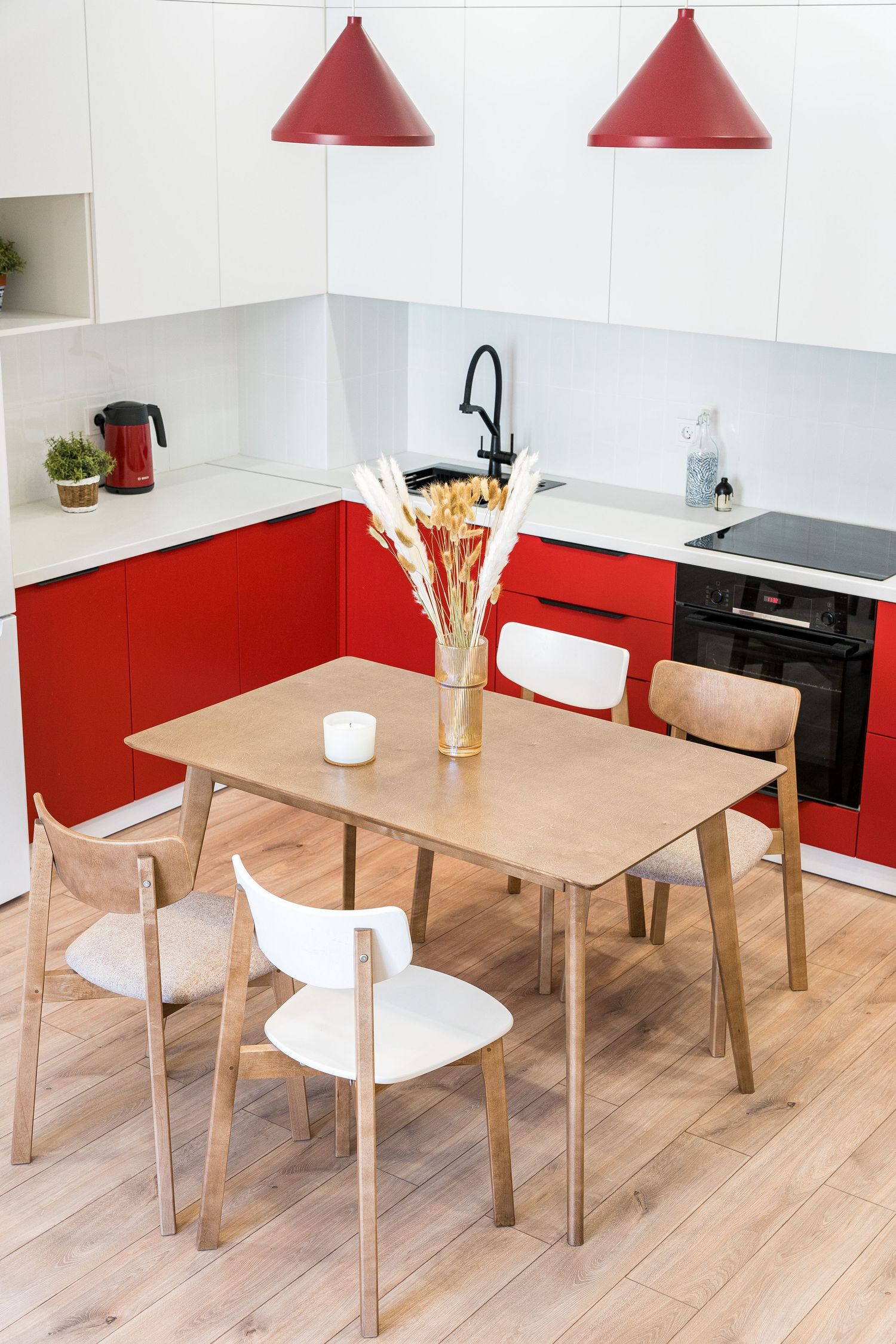 Modern red and white kitchen with wooden dining set and conical red pendant lights.