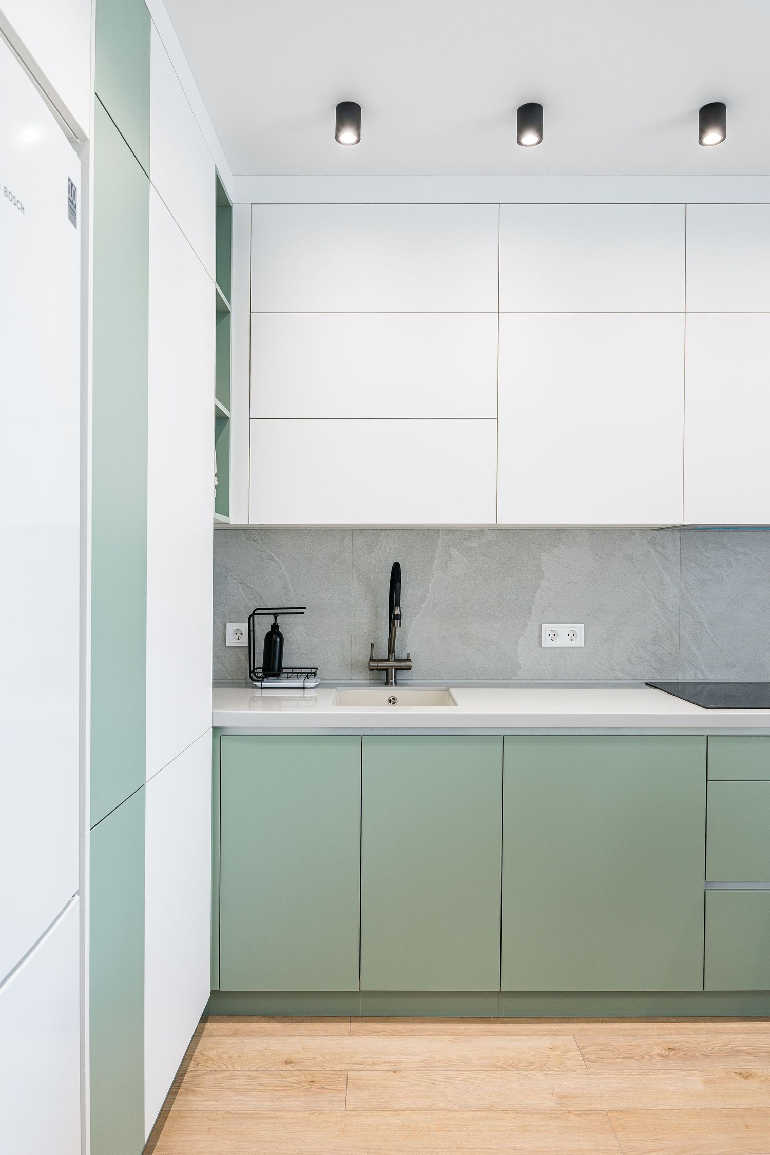 Minimalist kitchen featuring sage green lower cabinets and white upper cabinets with black fixtures.
