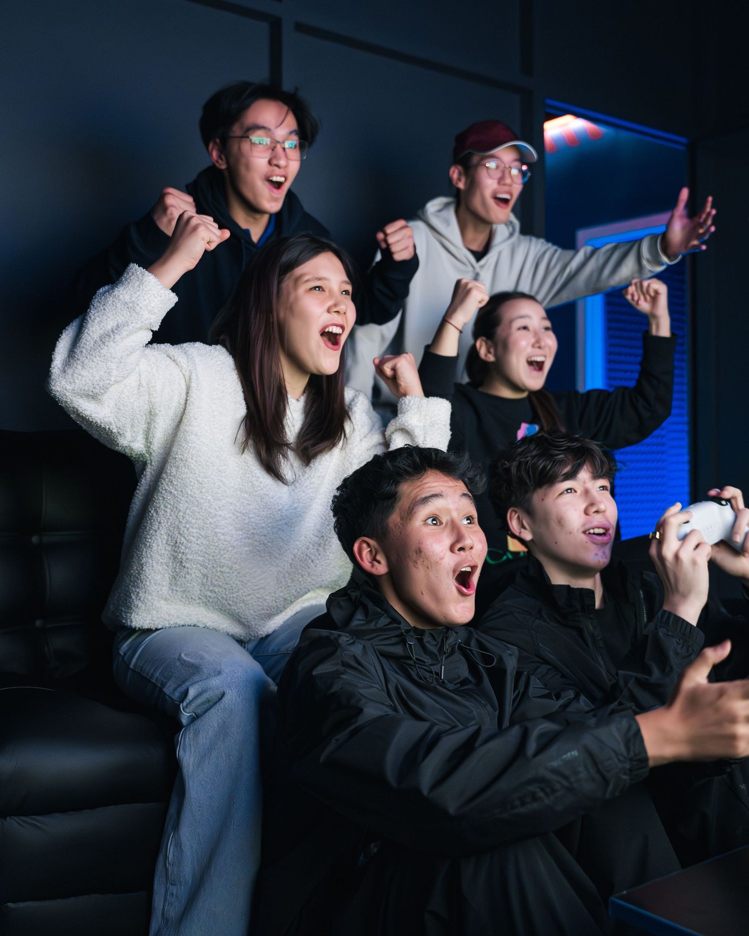 Friends reacting with excitement while playing competitive video games in a dimly lit gaming room.