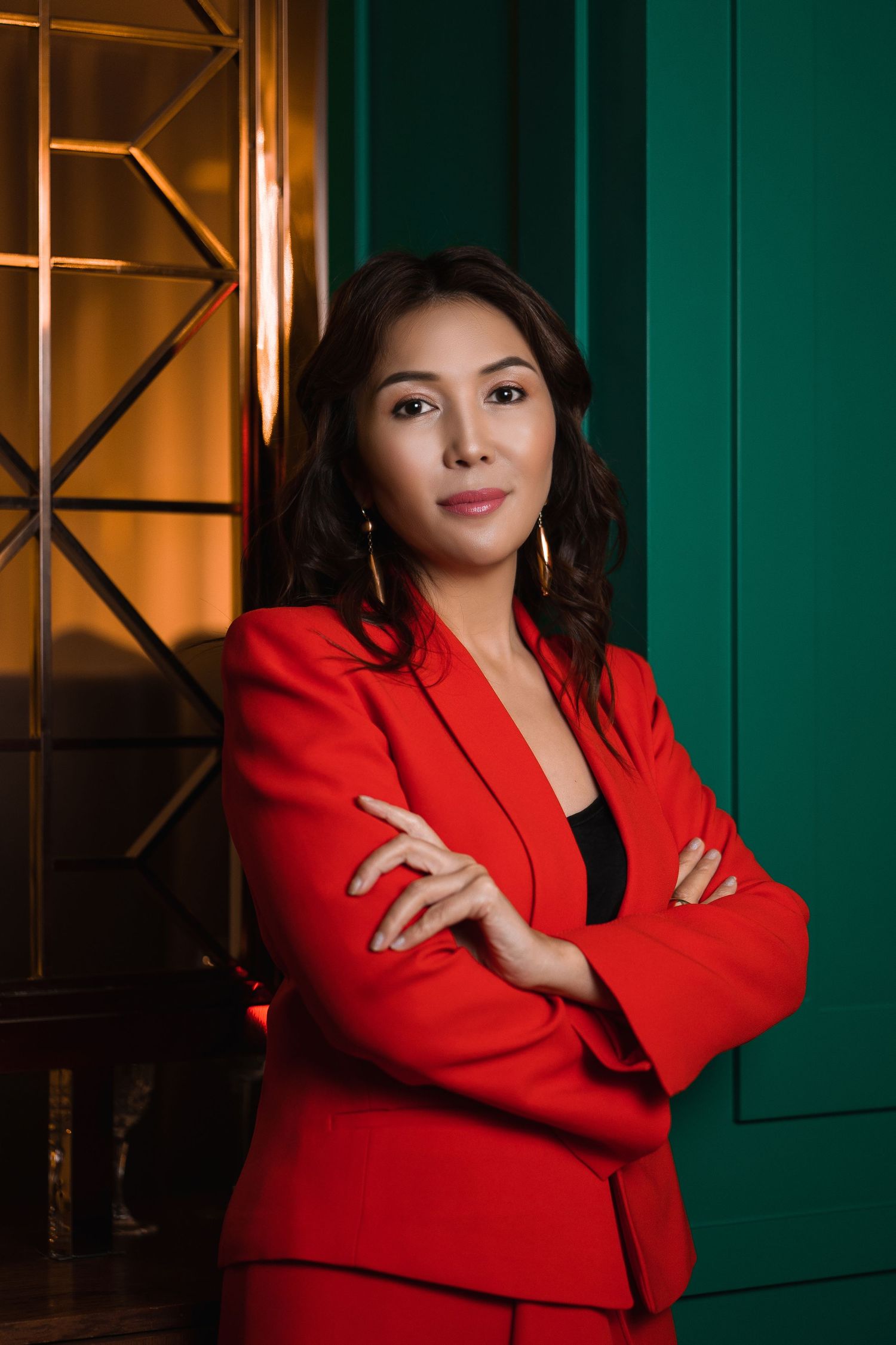 Professional portrait in vibrant red blazer against dark green background.