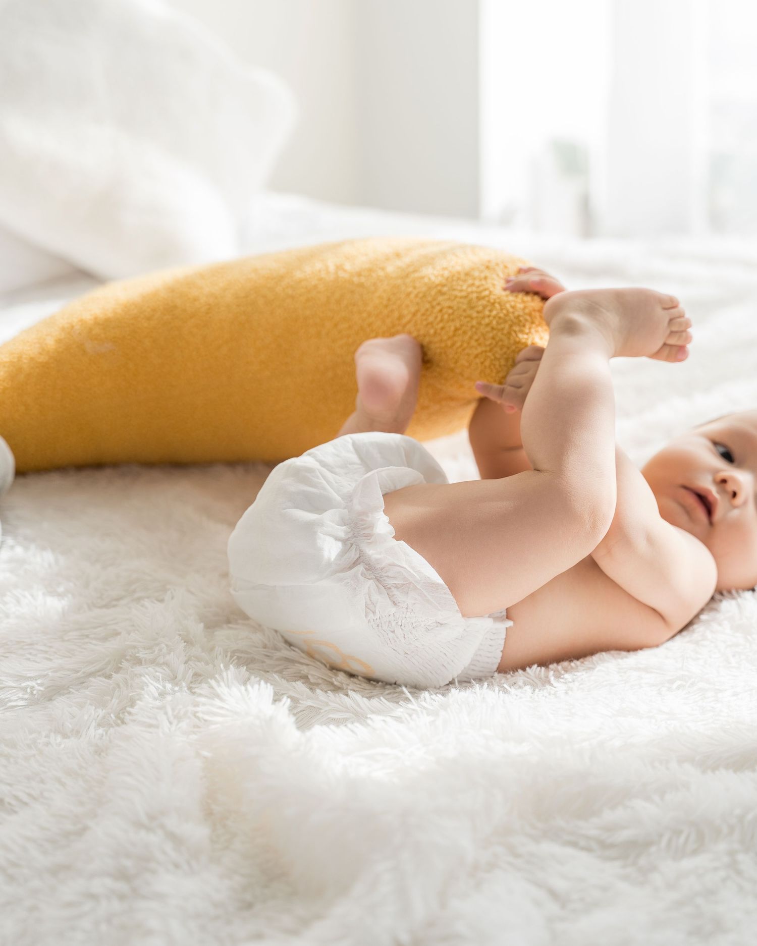 Infant in white diaper resting peacefully on plush white carpet.