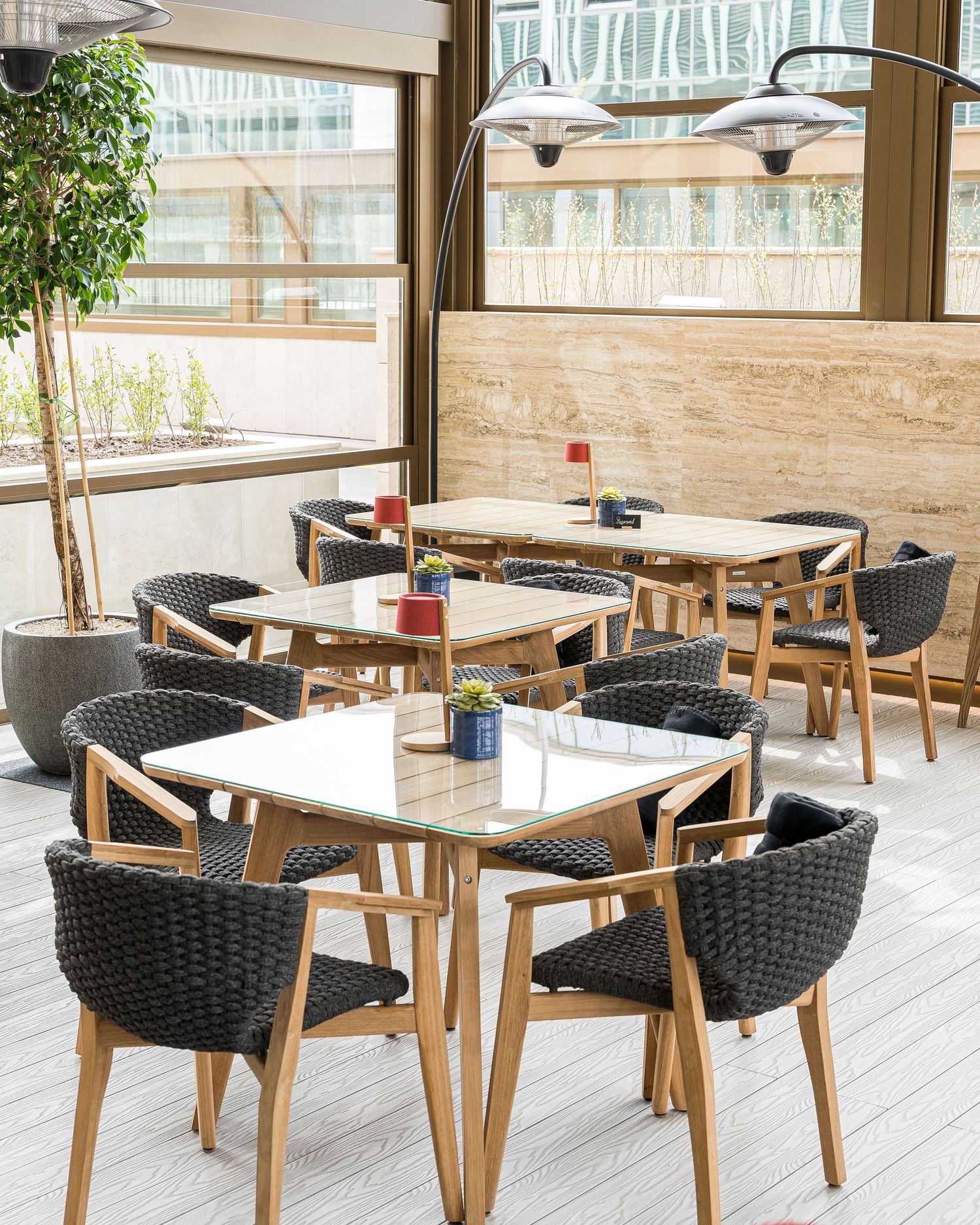 Restaurant seating area with woven black chairs and wooden tables in a bright sunlit space.