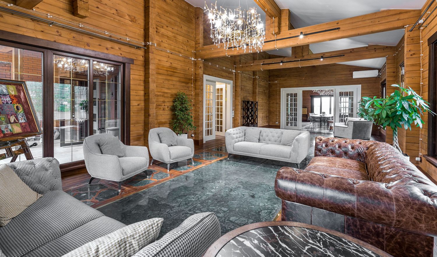 Rustic luxury lounge with exposed wooden beams, crystal chandeliers, and comfortable gray seating.