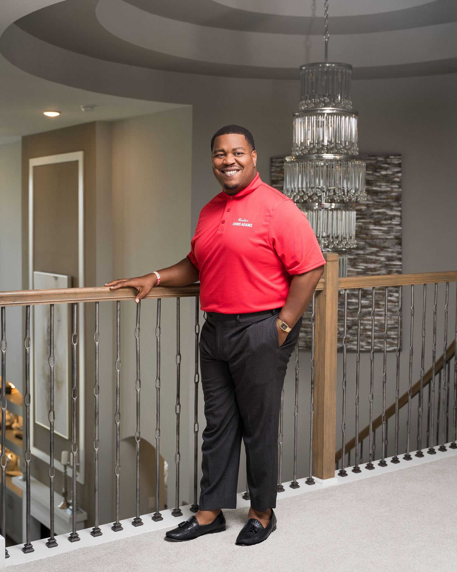 Individual in red polo shirt posing by modern staircase with metal railings.