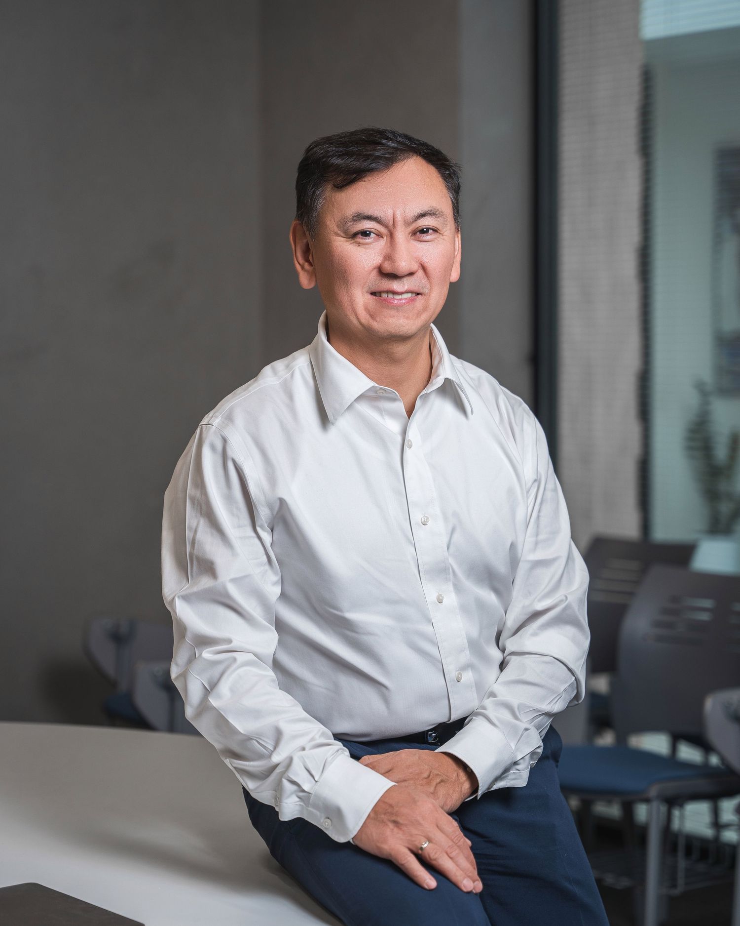 Professional headshot in white dress shirt against modern office background.