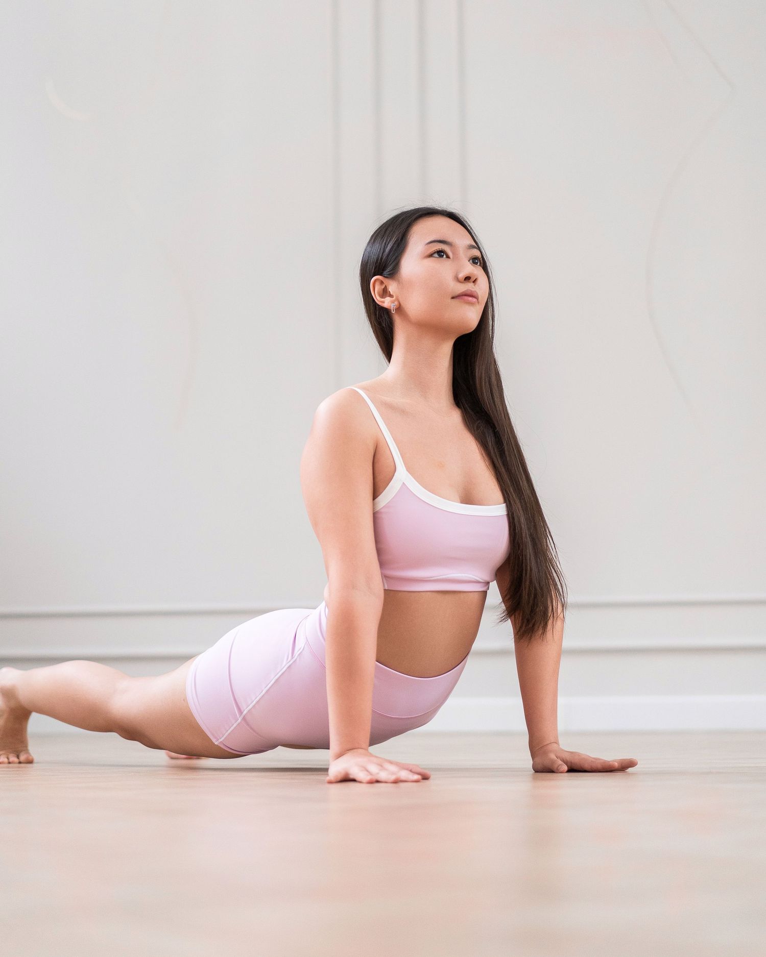 Yoga practitioner demonstrating cobra pose on light wooden floor.