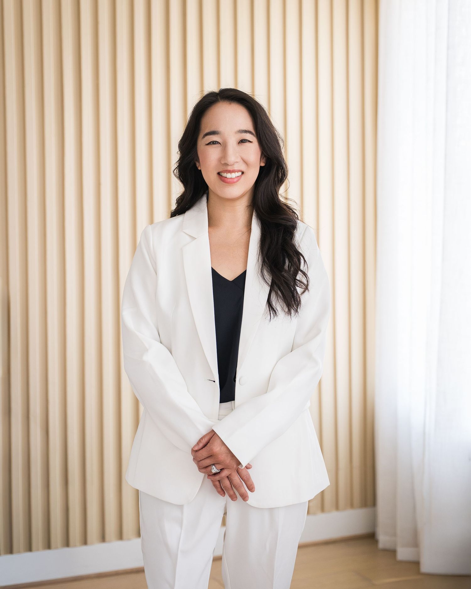 Professional in crisp white blazer and black top standing in modern office setting.
