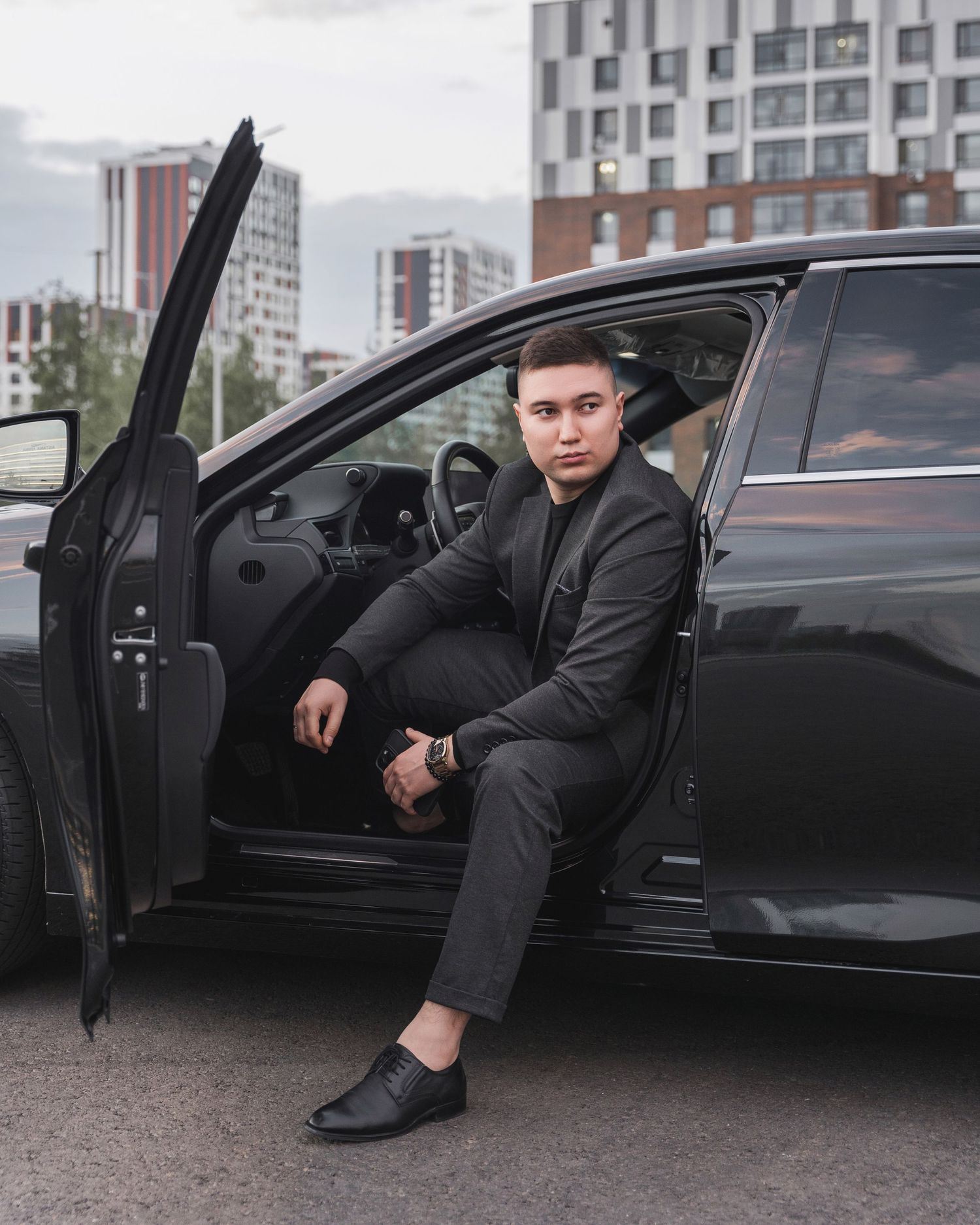 Professional poses with black luxury vehicle in urban setting.