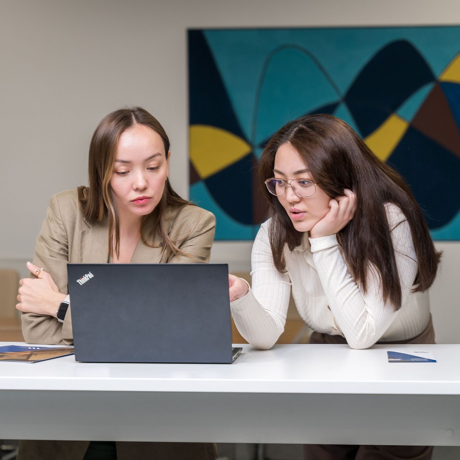 Professional working on laptop in office setting with geometric wall art in background.