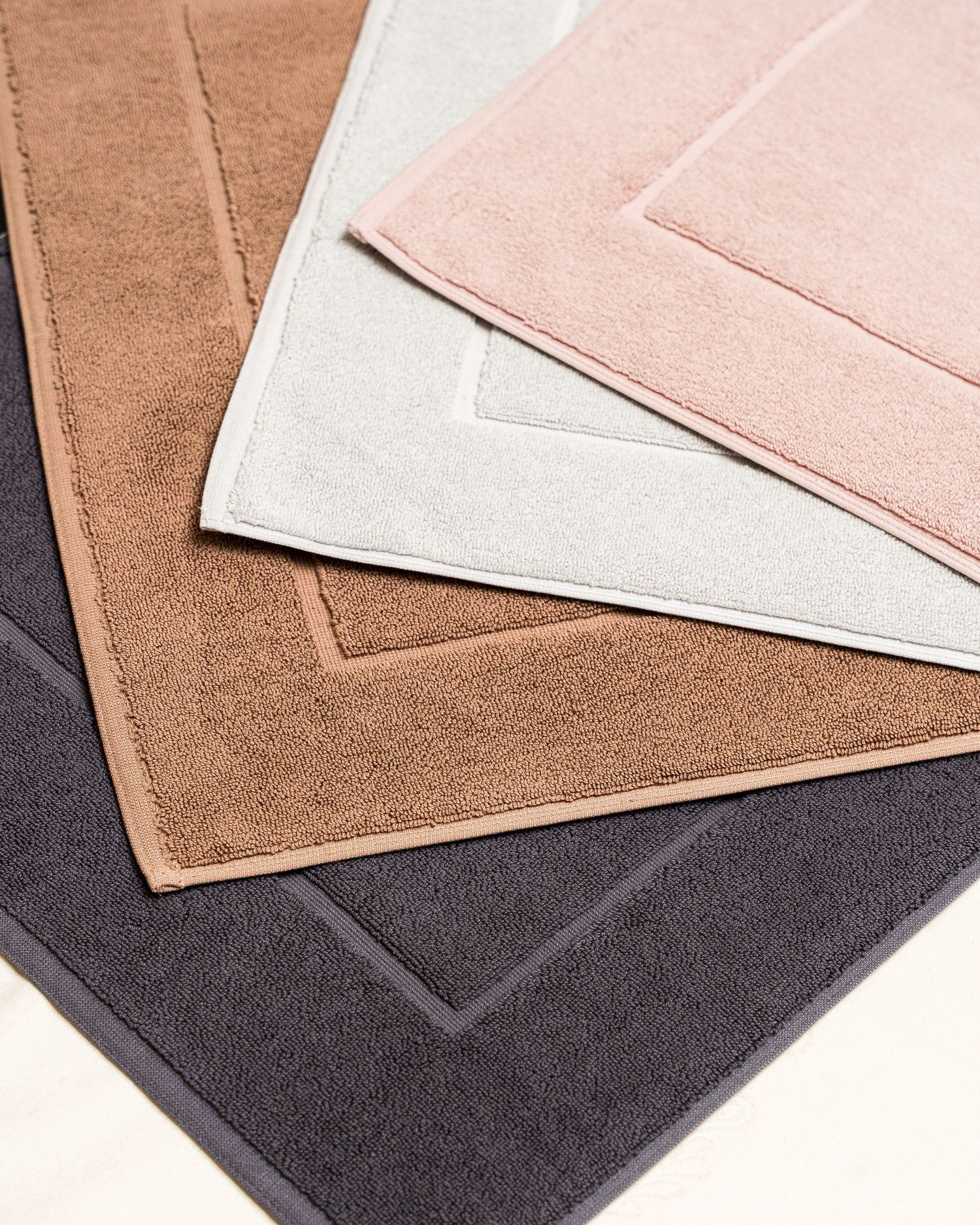 Collection of bath mats in neutral tones including white, pink, tan and charcoal gray.