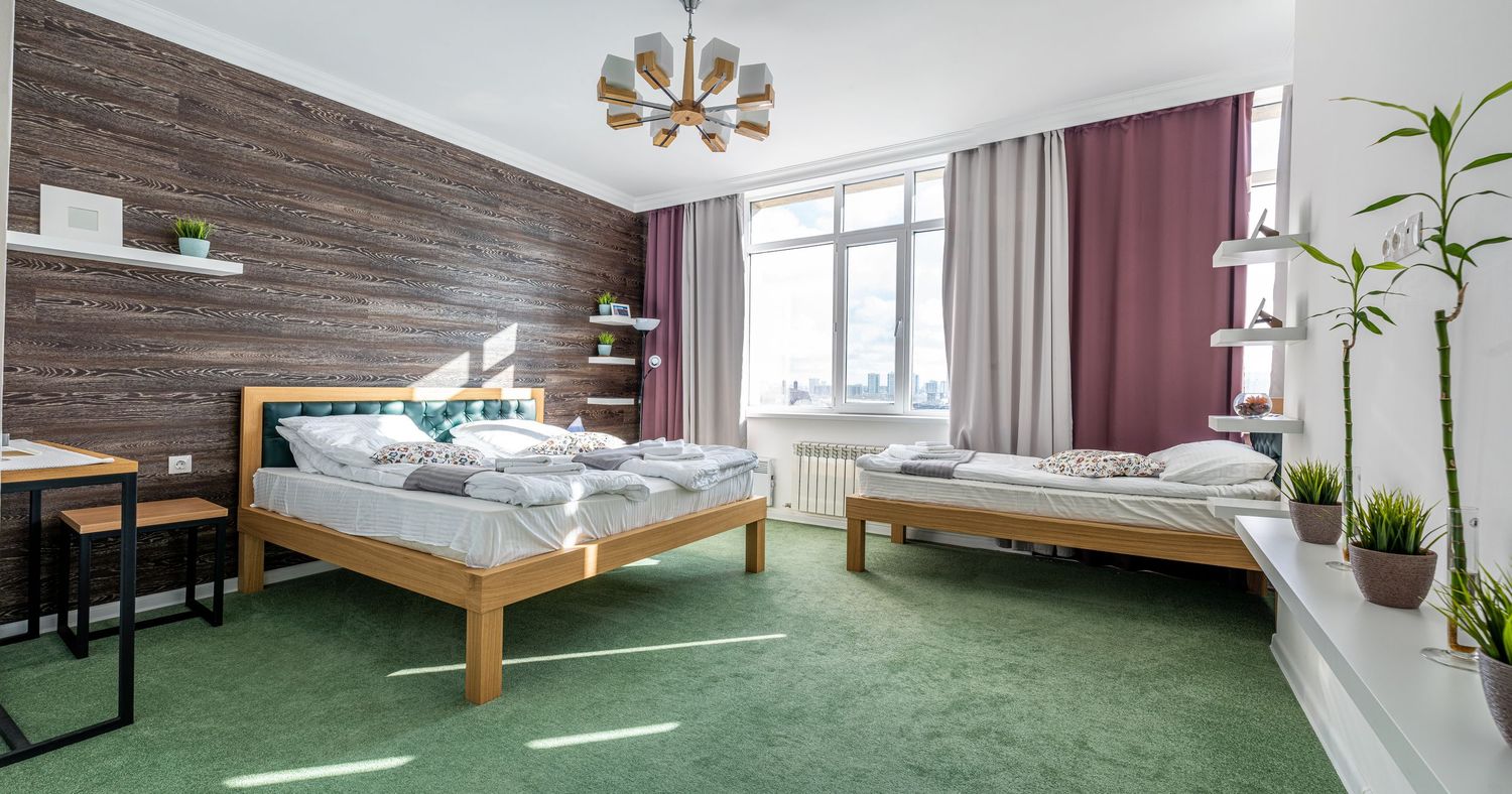 Spacious hotel room with wooden walls and green carpet showing multiple angles of the bed and seating area.