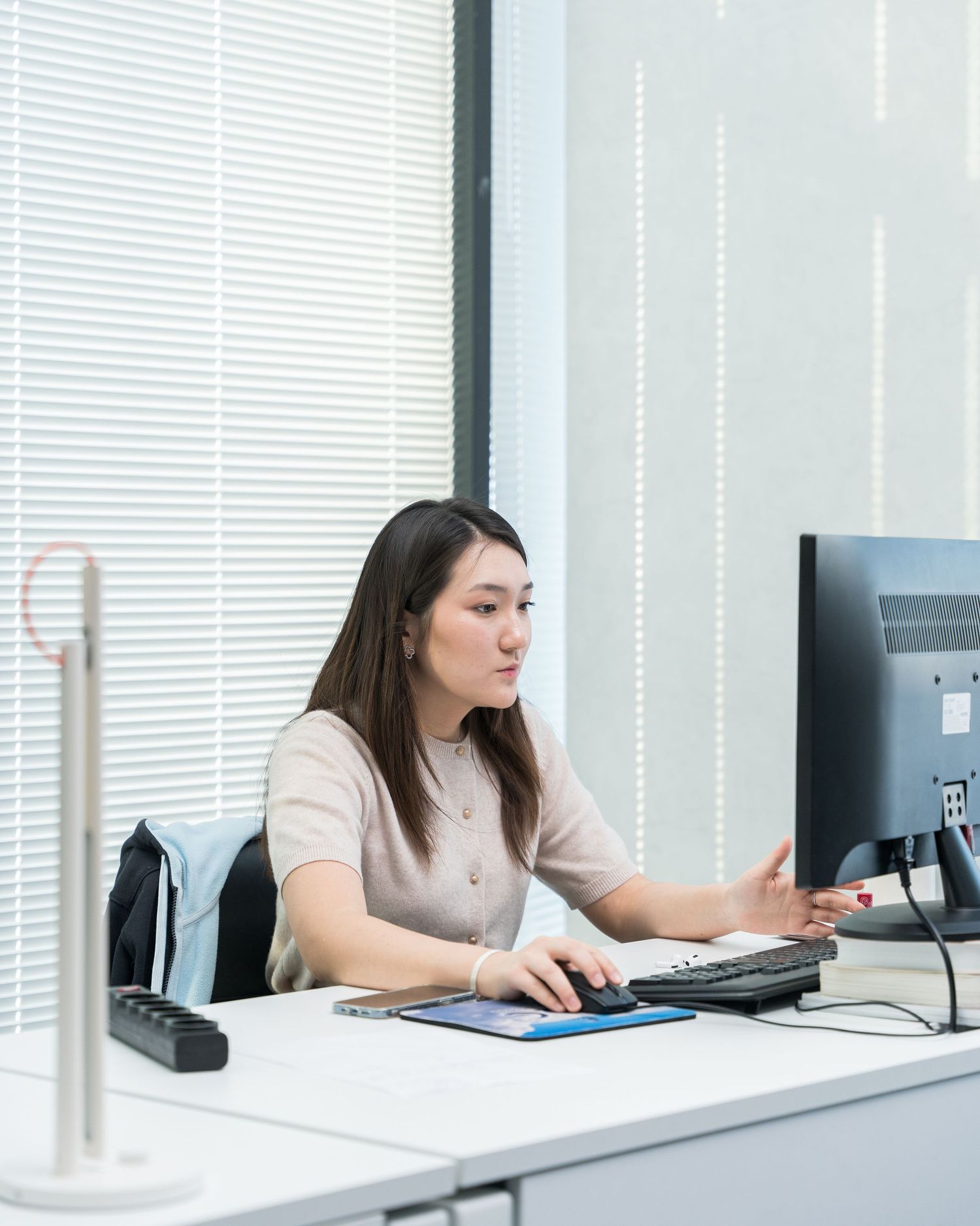 Professional working at a computer desk with a phone and monitor in a bright office space.