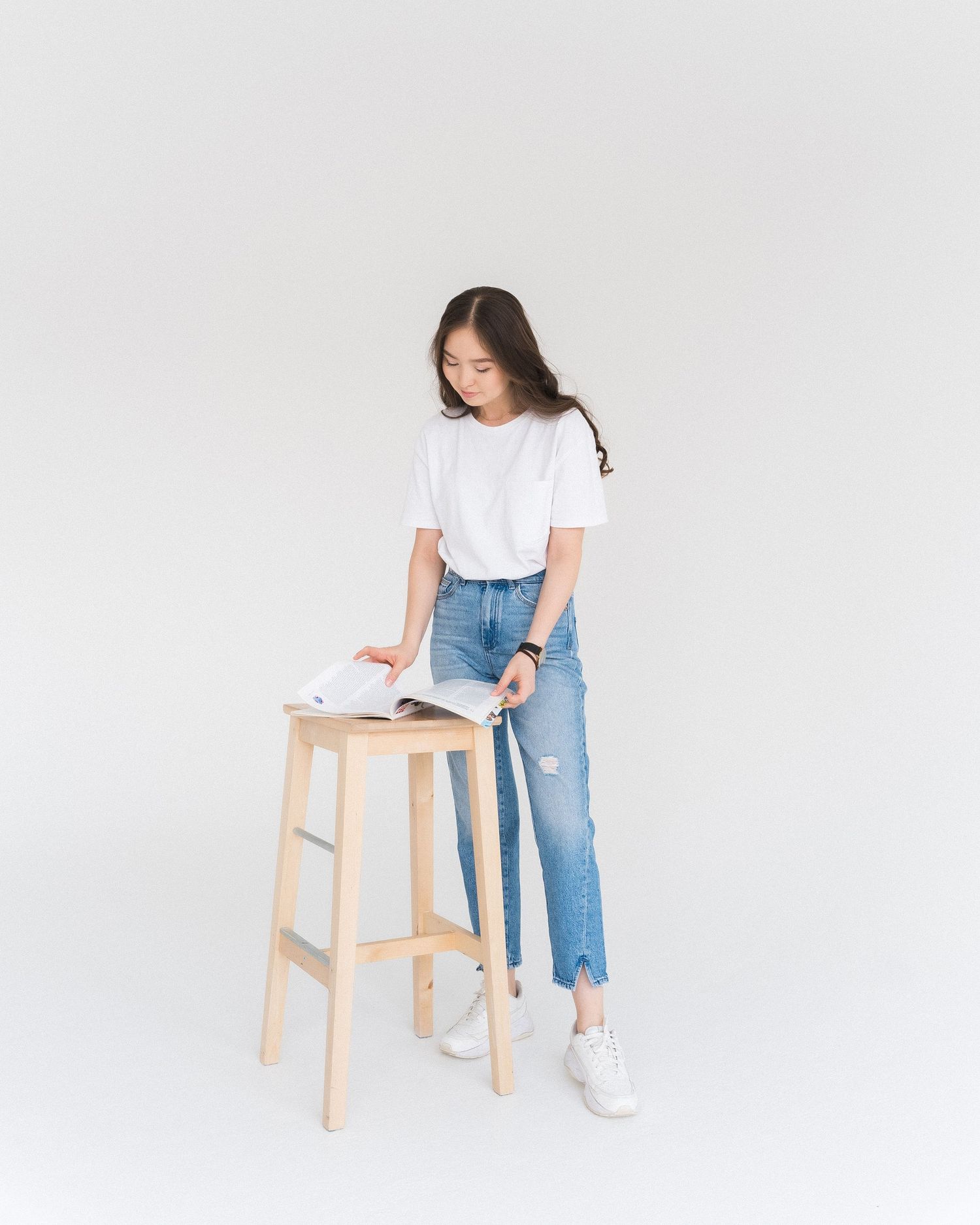 Person in casual wear sitting on wooden stool against white background.