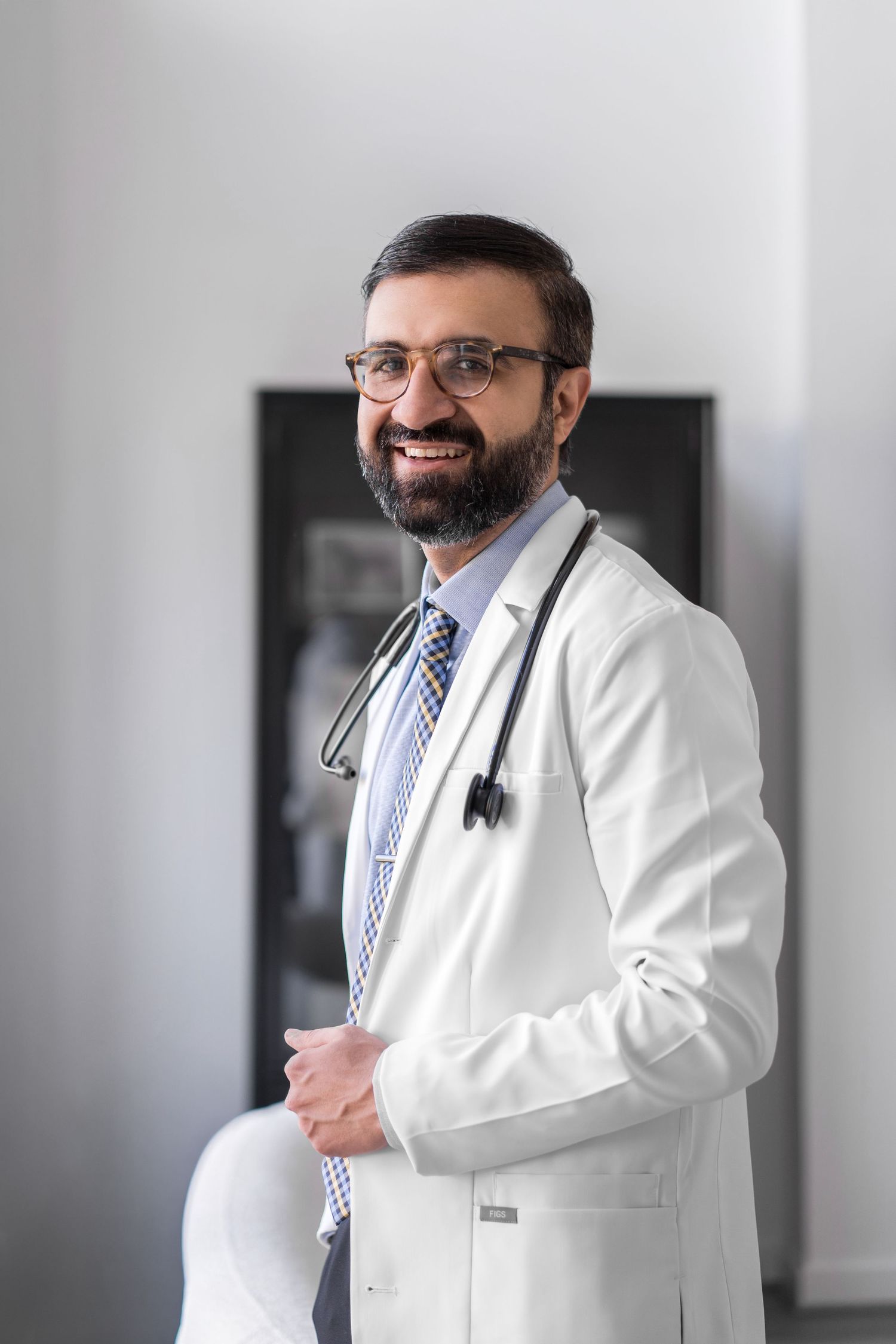 Medical professional in white coat and tie standing in clinical setting.