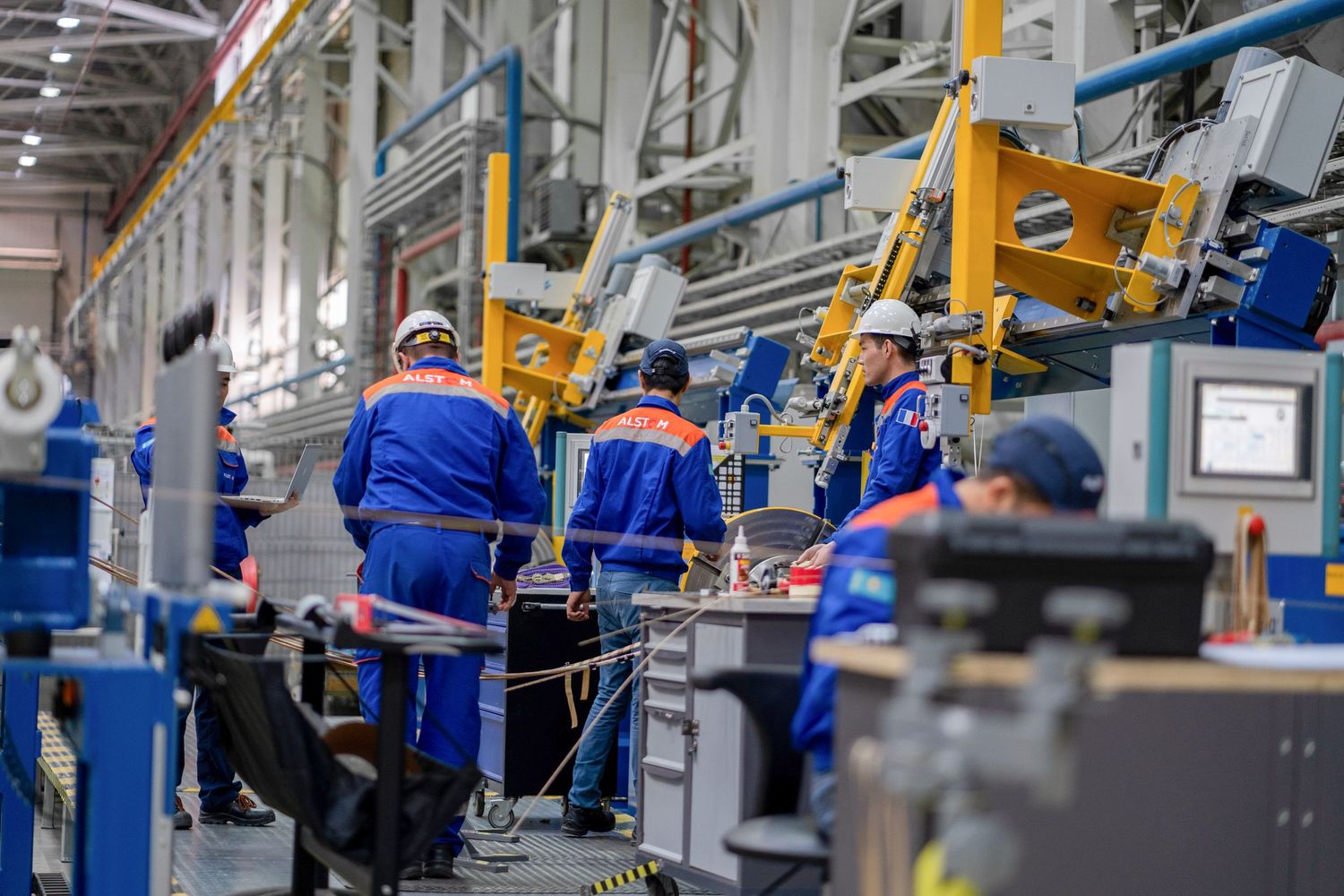 Industrial production line showing workers in blue uniforms operating manufacturing equipment.