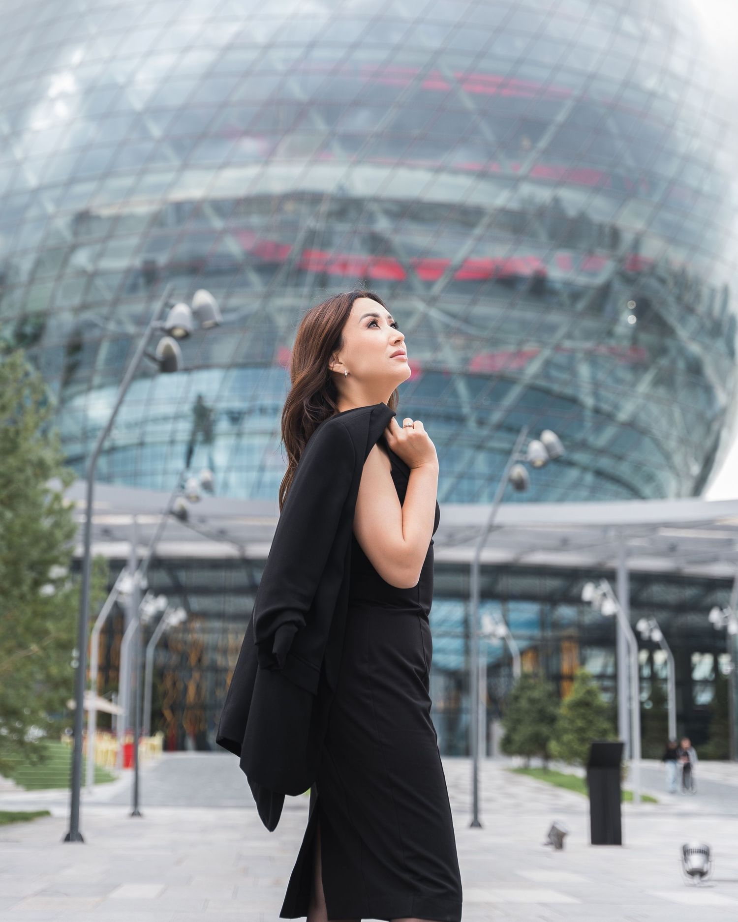 Person in black outfit photographed against modern glass architecture background.
