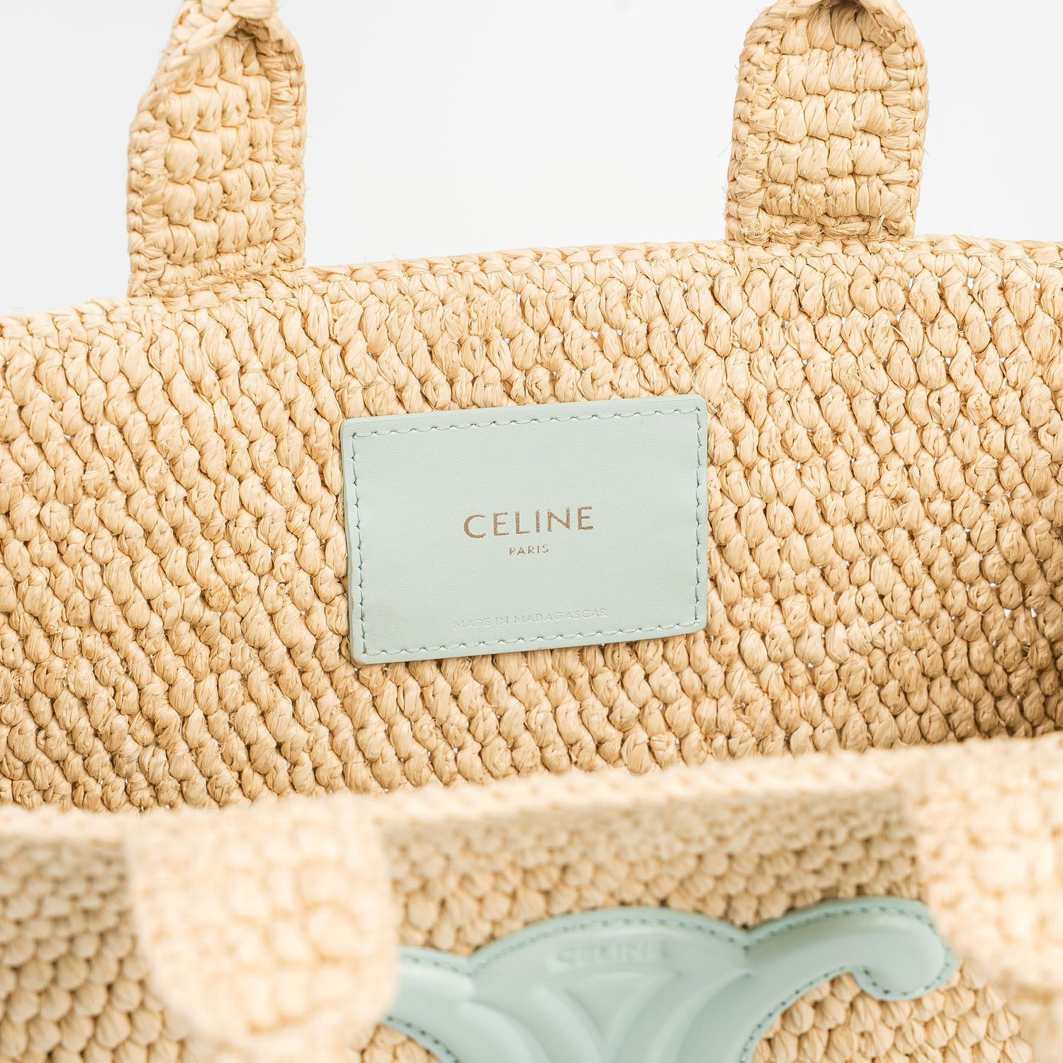 Close-up details of a beige Celine straw bag showing brand label and texture.