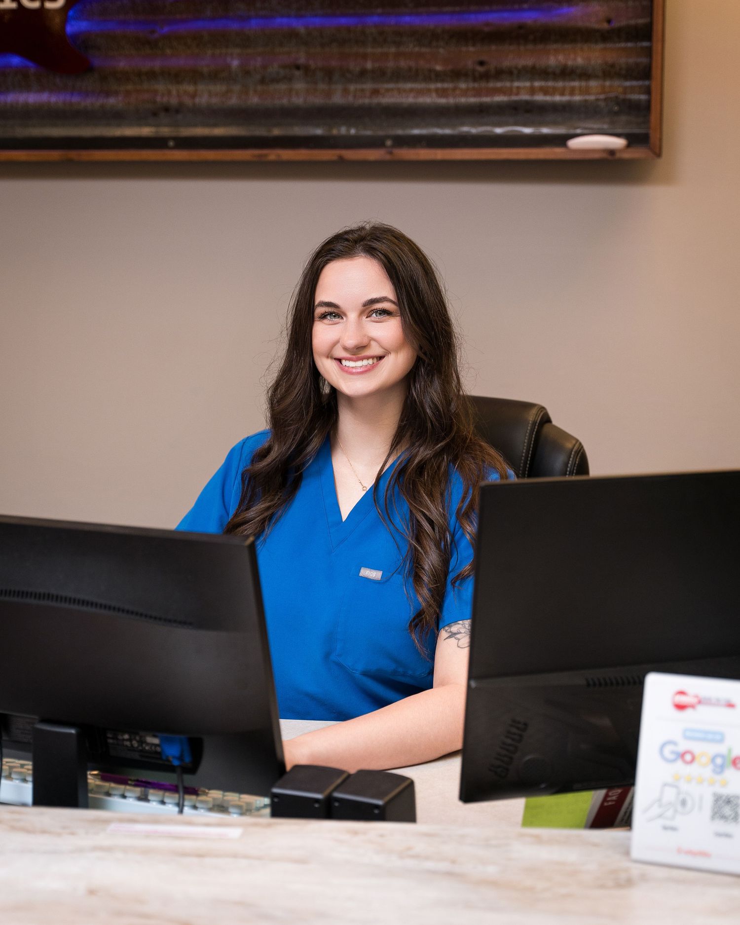 Medical professional in blue scrubs working at front desk reception area.