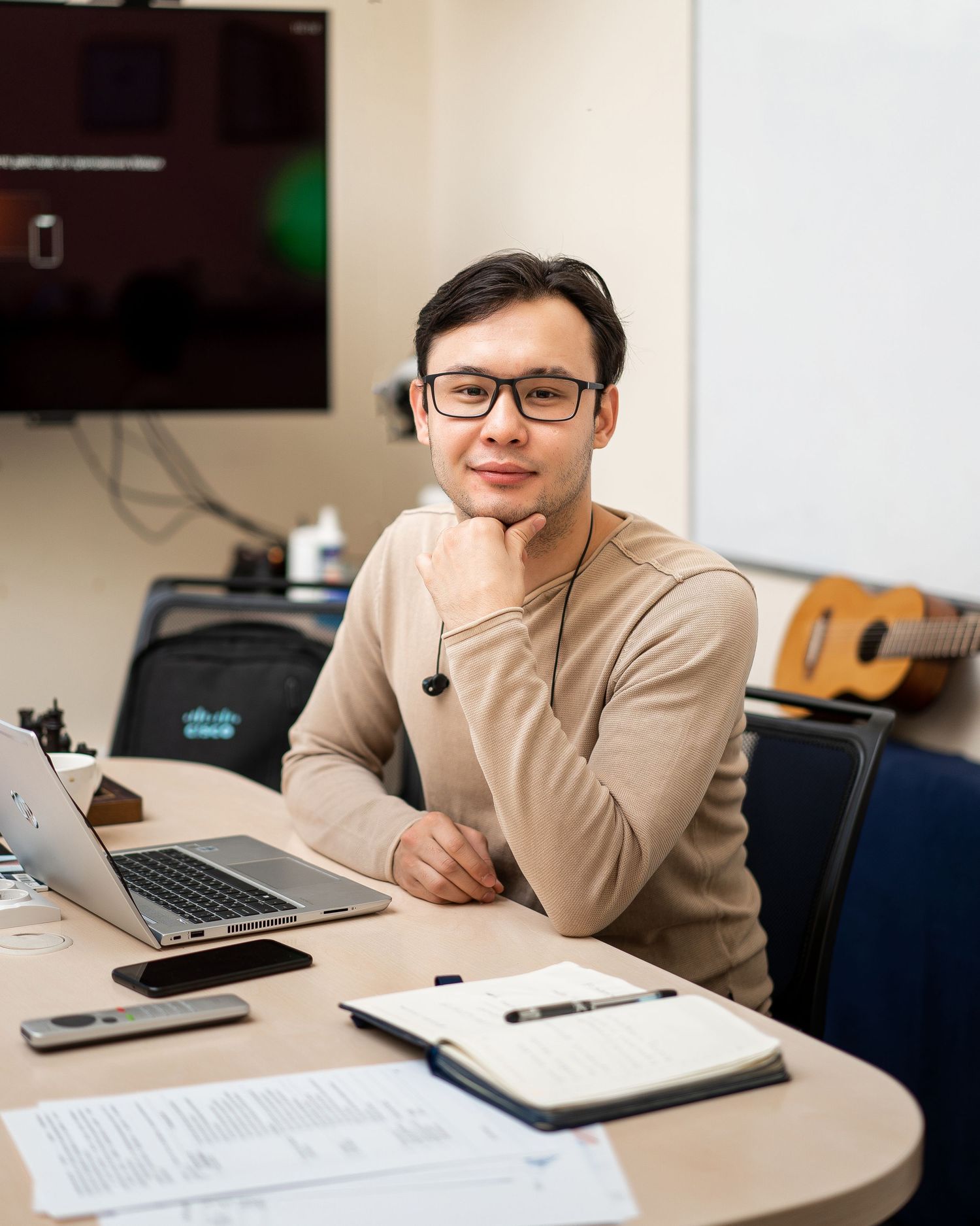 Professional in beige sweater working on laptop and taking notes in modern office setting.