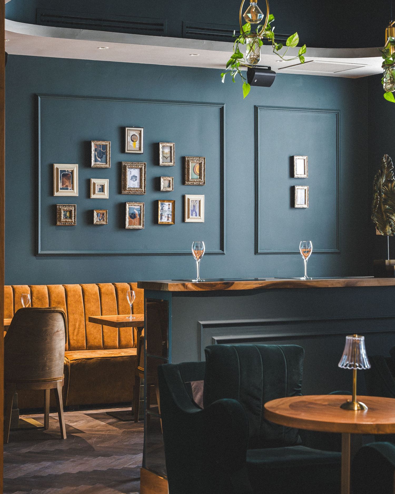 Cozy restaurant interior with teal walls, vintage photo frames, and orange velvet banquette seating.