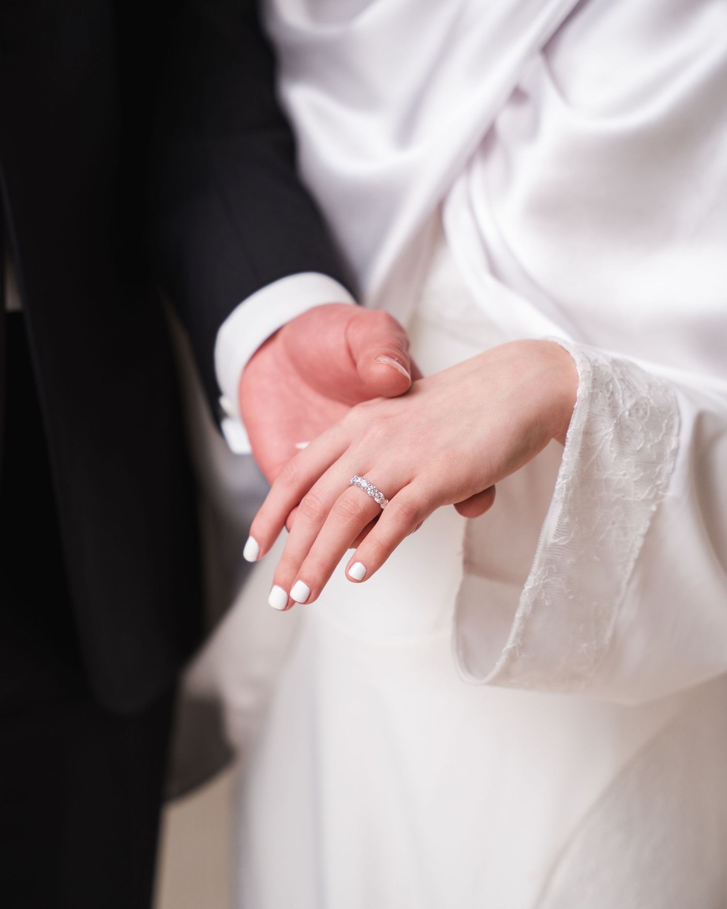 Close-up of a bride's hand with white nails and diamond ring resting on groom's arm in black suit.